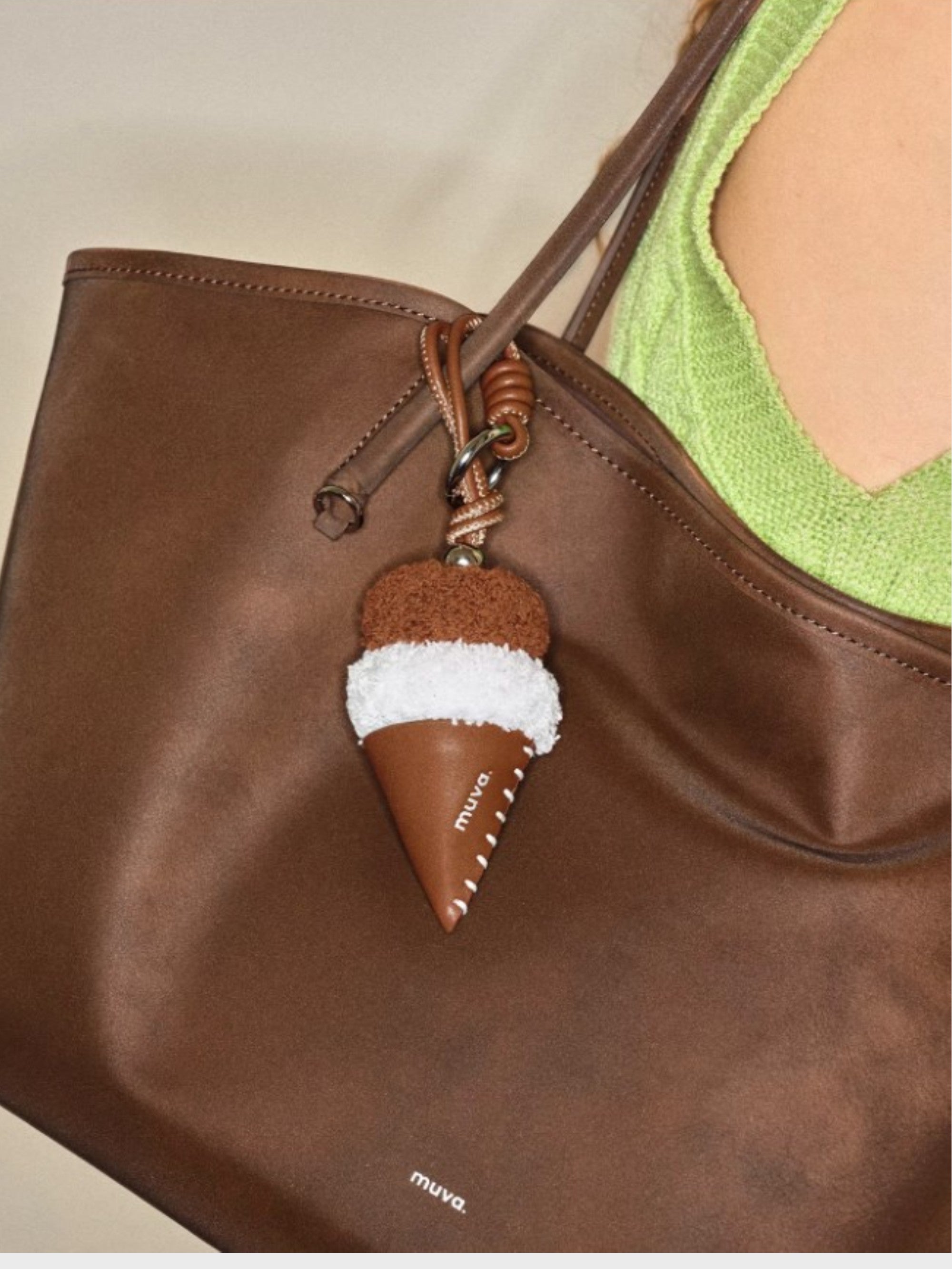 Breloque de sac Crème glacée duveteuse MUVA accrochée à un sac en cuir marron.
