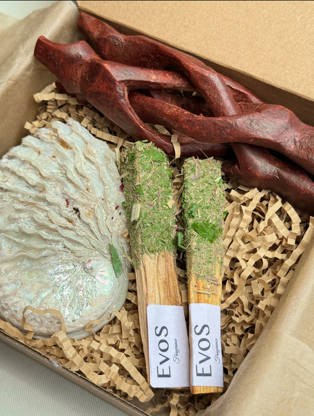 Coffret cadeau EVOS Fragrance avec deux bâtons de palo santo aux herbes séchées vertes, racine en bois rouge sculpté et savon nacré blanc, présentation sur papier kraft crêpé
