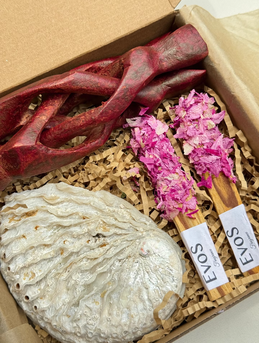 Coffret cadeau EVOS Fragrance avec deux bâtons de palo santo aux pétales de rose séchées roses, racine en bois rouge sculpté et savon nacré blanc, présentation sur papier kraft crêpé

