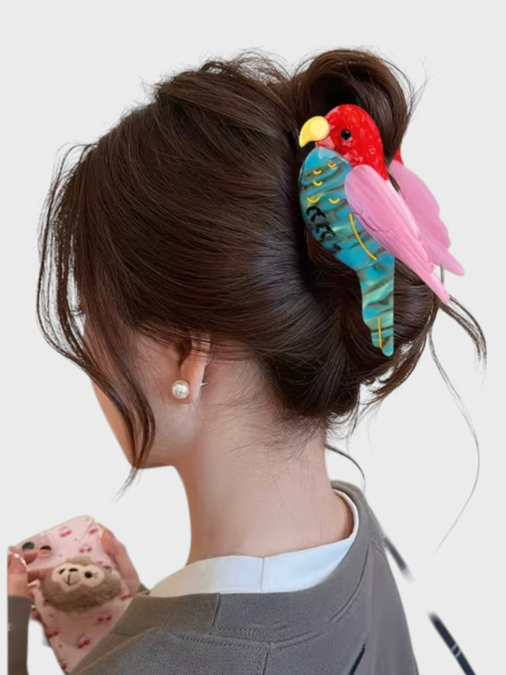 Pince à cheveux en résine DIOIB motif perroquet bleu, rose et rouge, portée dans un chignon, vue de dos
