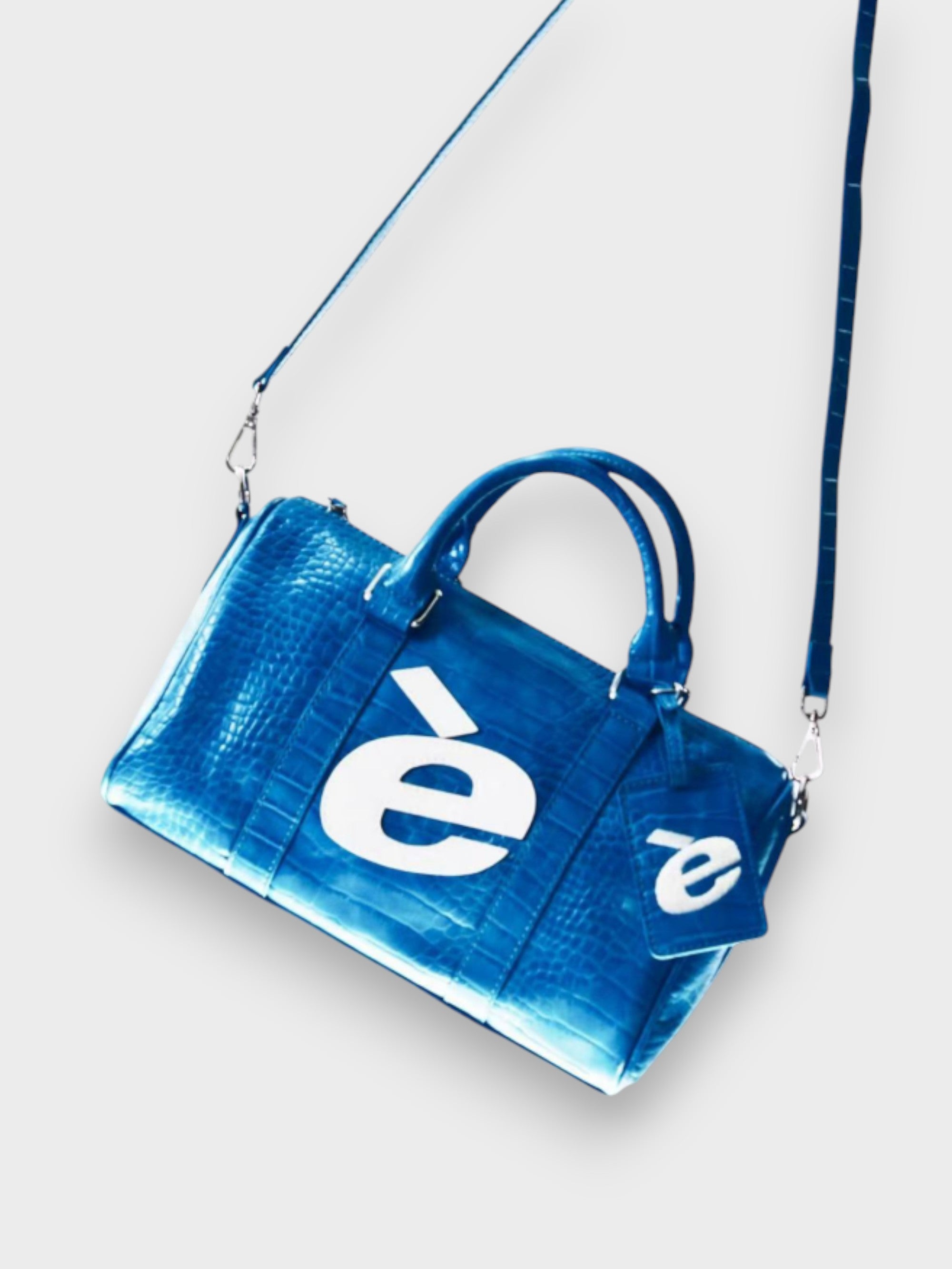 Sac bowling eeee Artmonster en cuir croco bleu électrique avec logo blanc et porte-monnaie assorti, vue de dessus en angle sur fond blanc
