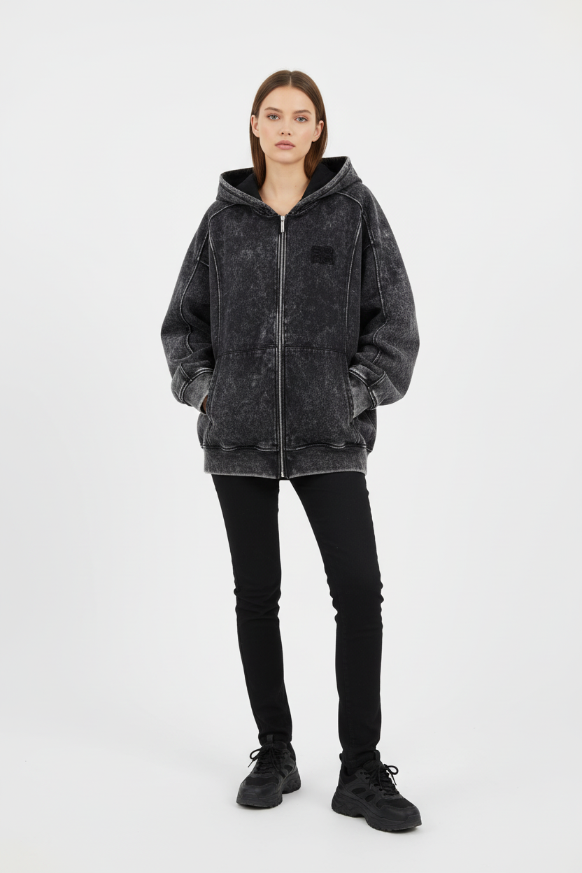 Sweat à capuche zippé oversize BJHG noir délavé avec patch logo, porté par une femme avec jean noir et sneakers noires, vue de face sur fond blanc
