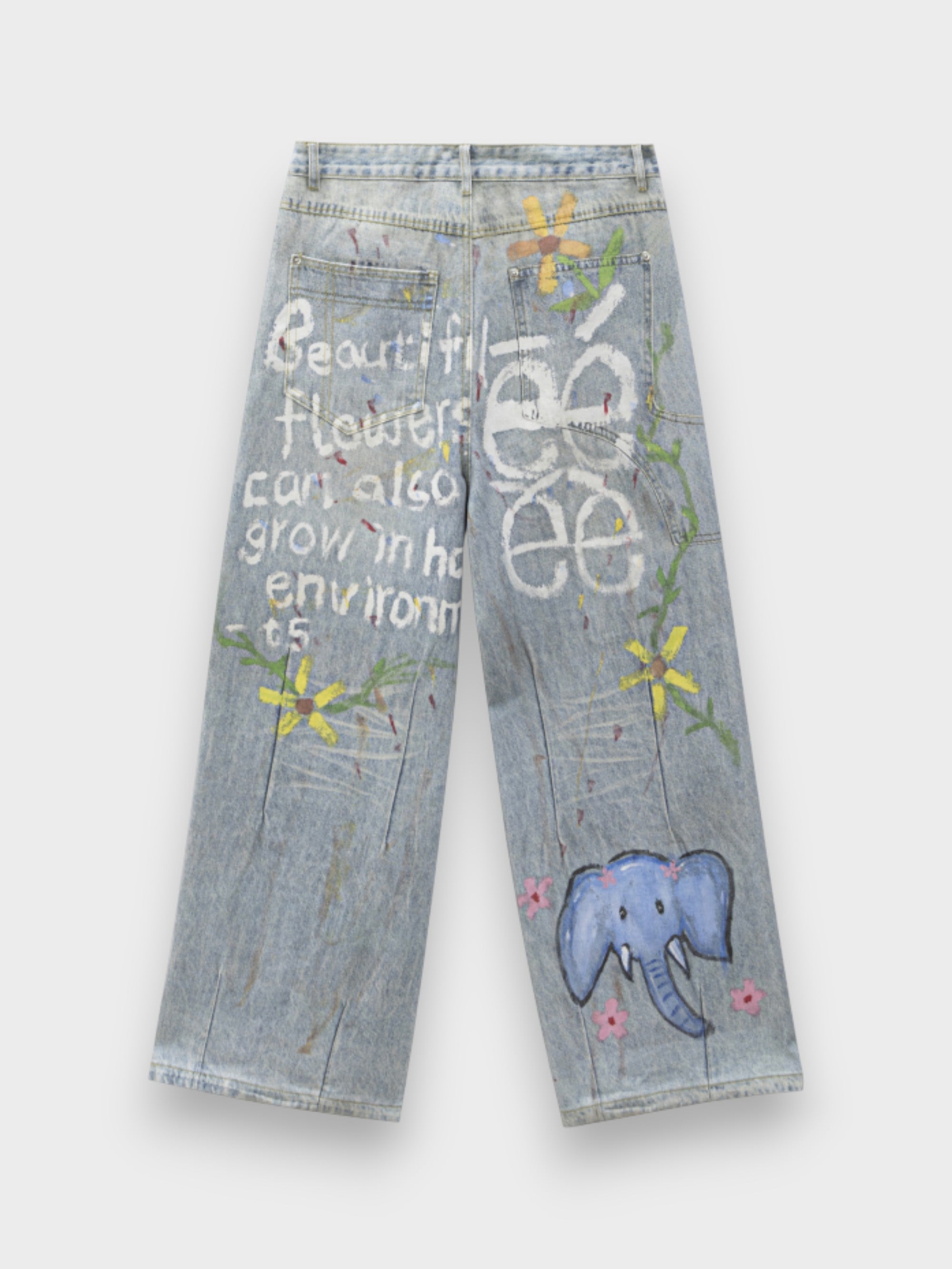 Jean large eeee Artmonster bleu clair avec prints graffiti éléphant bleu, fleurs jaunes et texte "Beautiful flowers can also grow in hard environments", vue de dos sur fond gris
