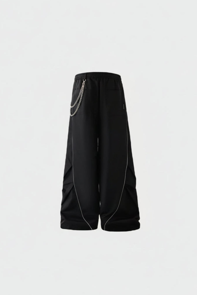 Pantalon large BJHG noir avec chaîne argentée à la ceinture et liserés blancs sur les jambes, vue de face sur fond gris

