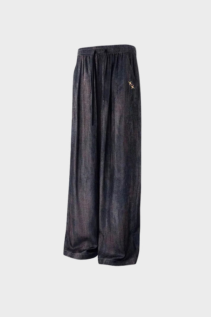 Pantalon large BJHG noir en satin à élastique ceinture avec broderie étoile dorée, vue trois quarts sur fond gris
