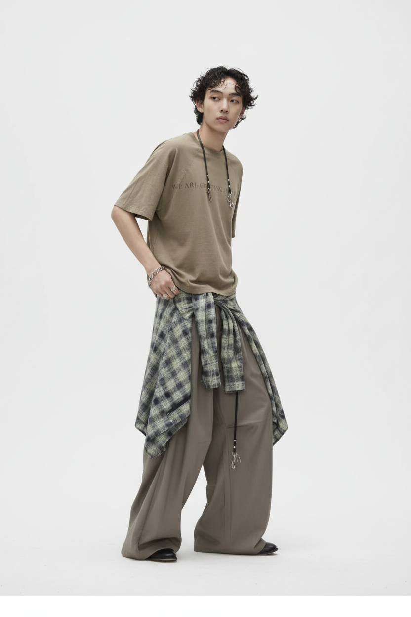 Pantalon large à plis RELABEL beige oversize, porté par un homme avec chemise à carreaux nouée à la taille, vue de face sur fond blanc