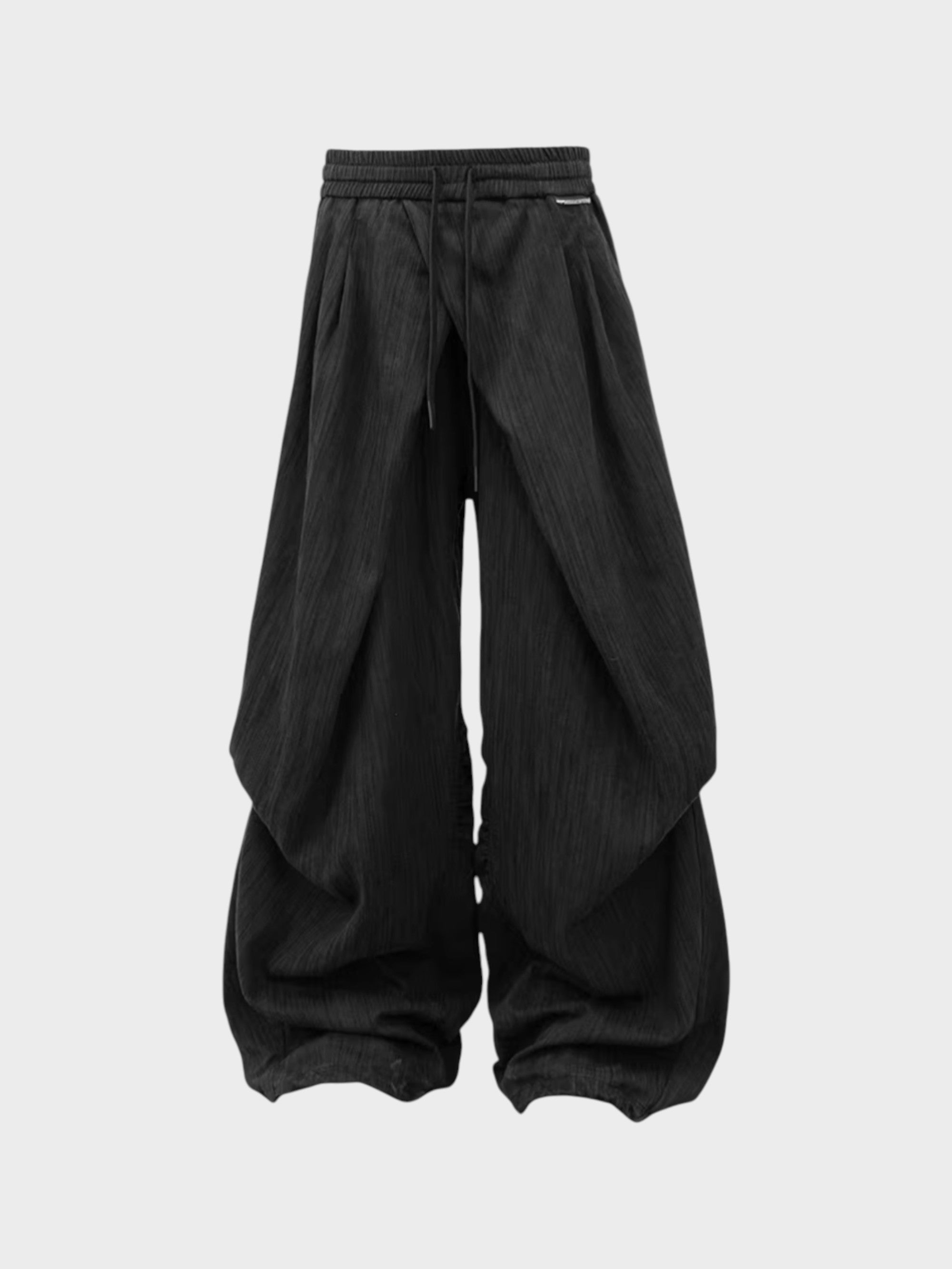 Pantalon sarouel RELABEL noir large à grands plis et cordon de serrage, étiquette métal, vue de face sur fond gris
