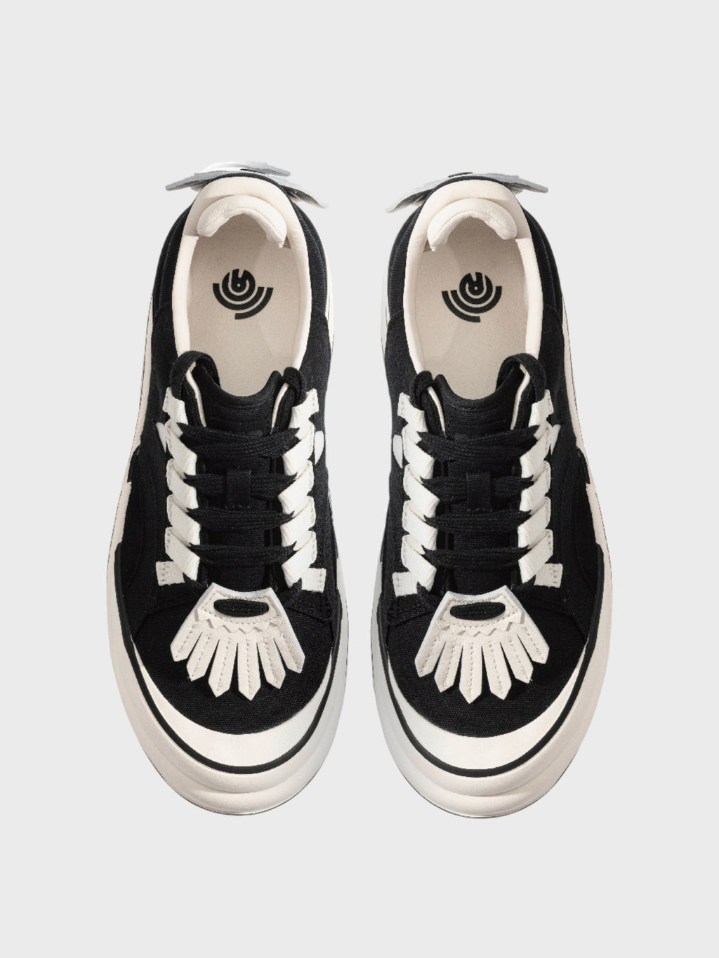 Radar Homing Beacon RHB sneaker – paire de sneakers daim noir lacets blancs plats, patch bout de pied blanc motif soleil éventail, logo œil concentrique intérieur, languette blanche, vue de dessus, fond gris clair
