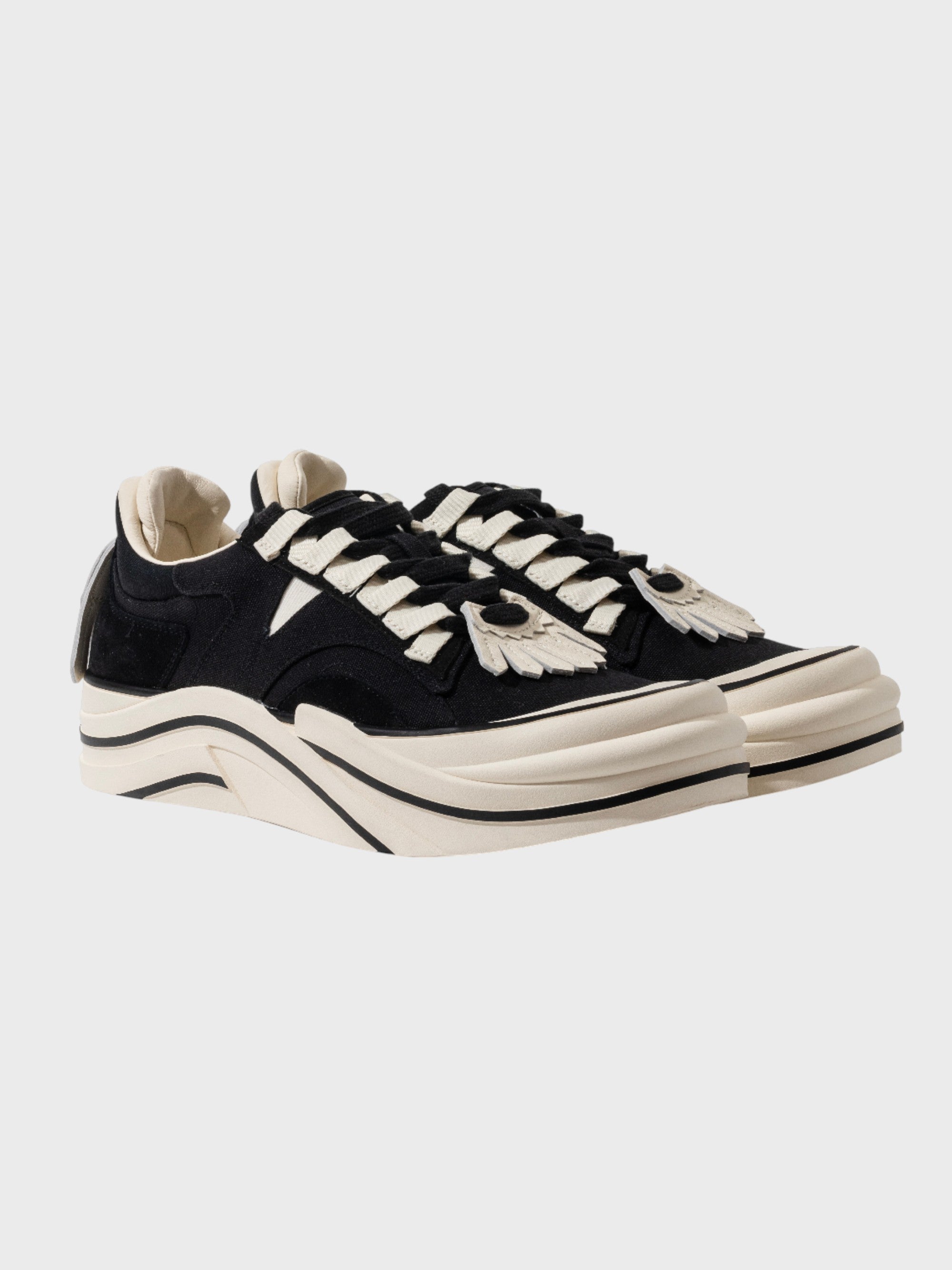 Radar Homing Beacon RHB sneaker – paire de sneakers daim noir lacets blancs plats, patch milieu pied blanc motif œil éventail, semelle épaisse blanche ondulée multi-couches, vue trois quarts avant, fond gris clair
