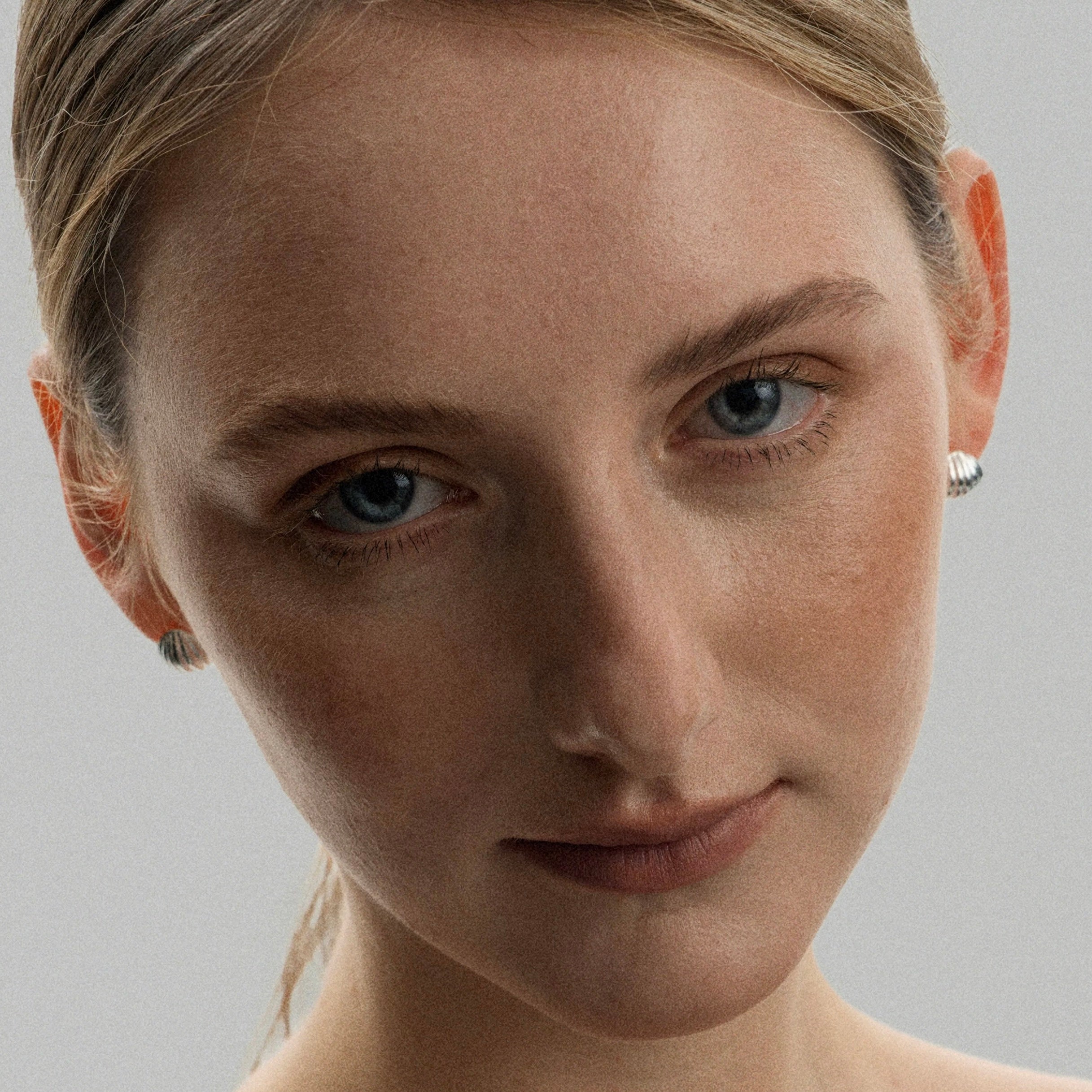 Boucles d'oreilles clou coquillage Freddo argentées en argent sterling, portées par une femme en studio, vue de face regard caméra