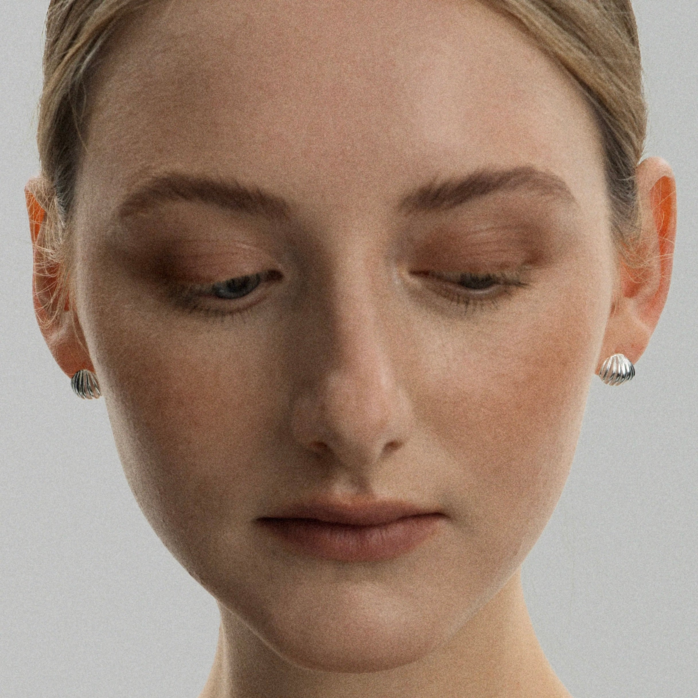 Boucles d'oreilles clou coquillage Freddo argentées en argent sterling, portées par une femme en studio, vue de face yeux baissés