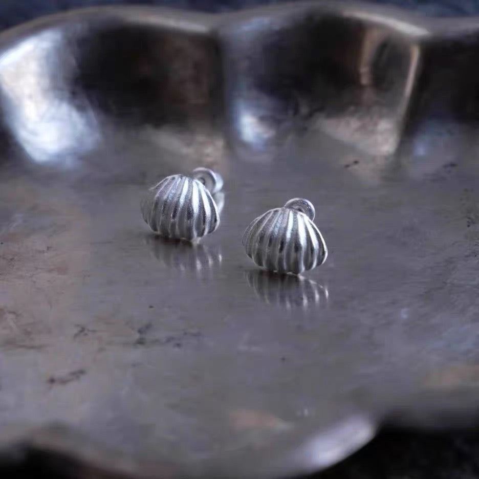 Boucles d'oreilles clou coquillage Freddo argentées en argent sterling, posées sur un plateau en métal argenté, vue rapprochée