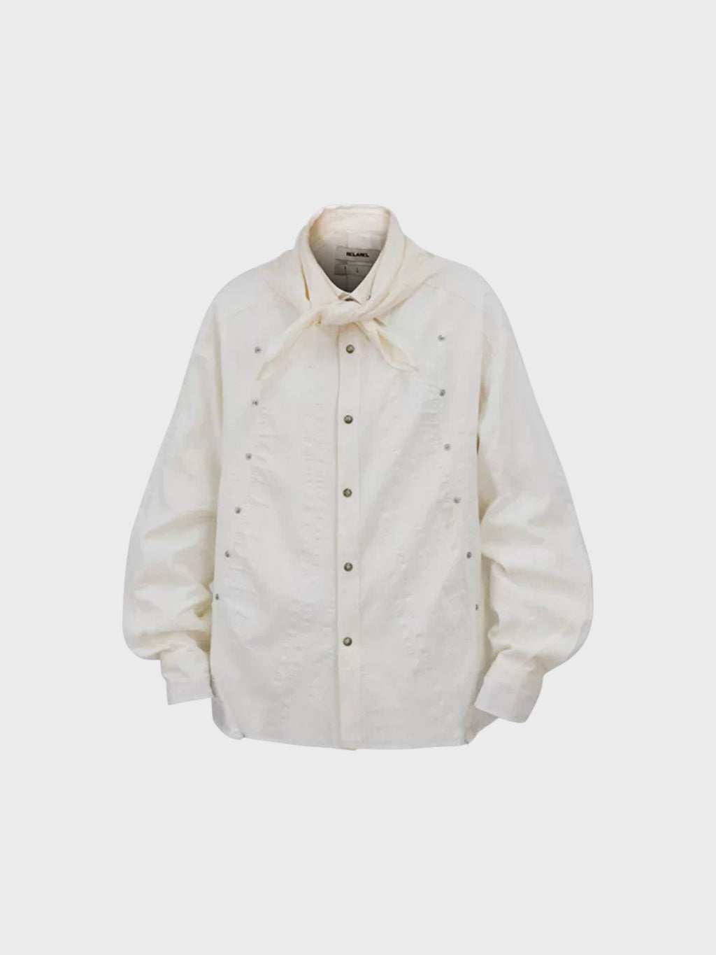 Chemise oversize RELABEL blanc cassé avec col foulard noué, rivets argentés all-over et boutons-pression, vue de face
