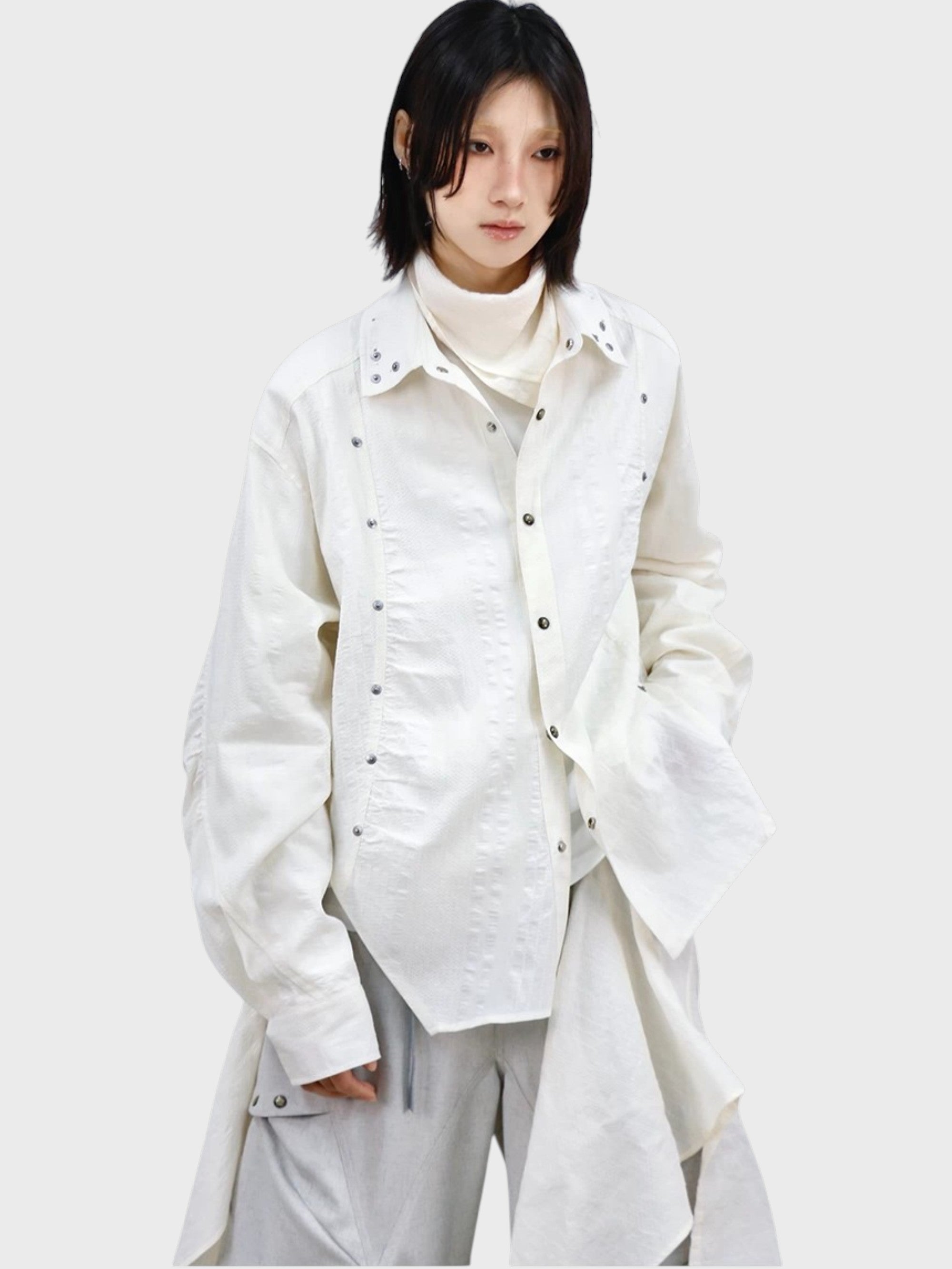 Chemise oversize RELABEL blanc cassé rivets argentés portée par une femme, vue de face avec col roulé blanc en dessous et pantalon large gris
