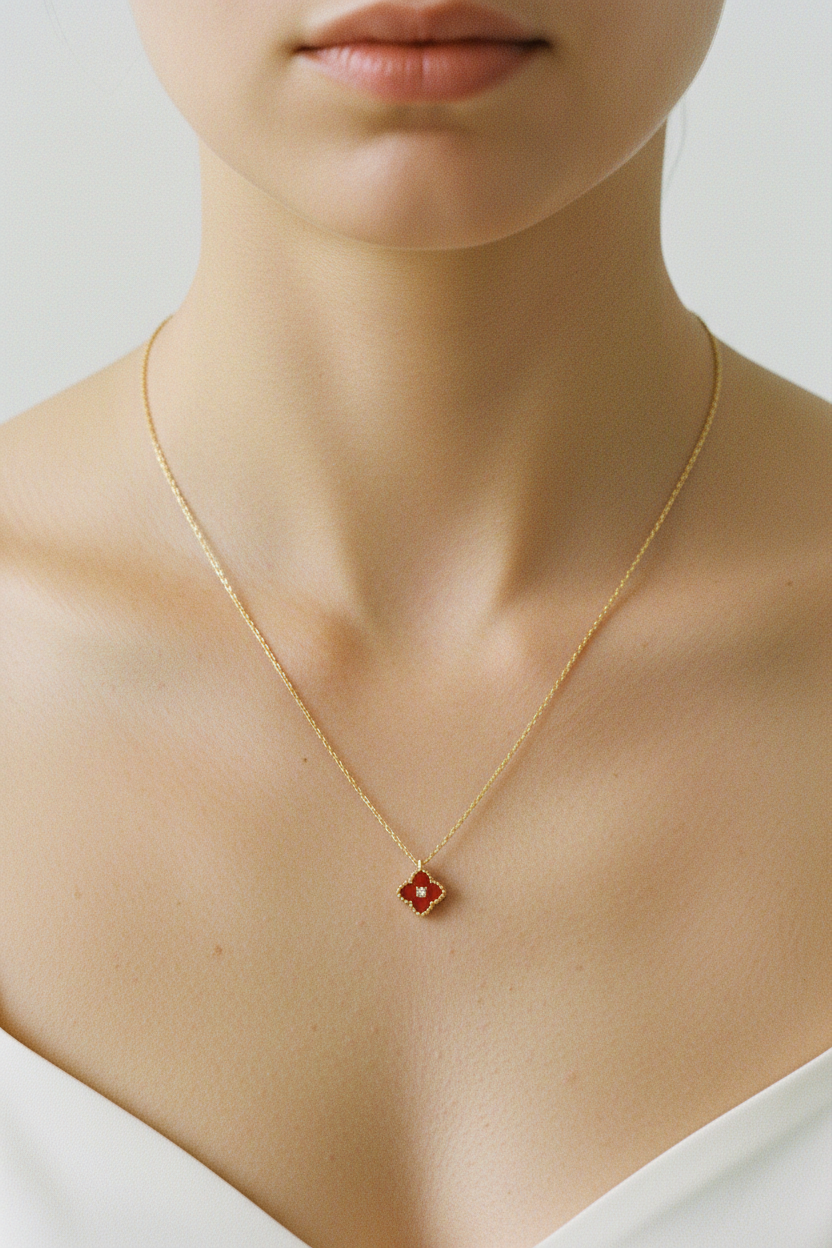 Collier pendentif trèfle FLV rouge et doré en métal doré et émail, porté par une femme décolleté blanc fond beige vue de face