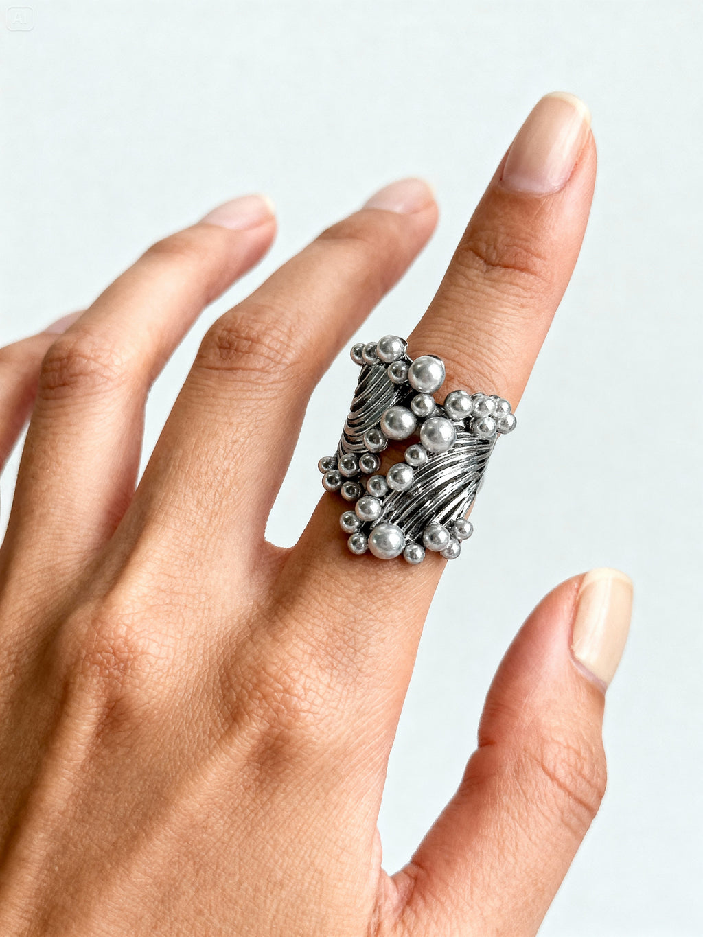 Bague design futuriste portée à la main, anneau argenté à reliefs et perles métalliques