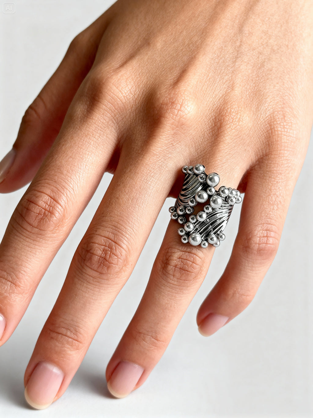 Gros plan d’une bague argentée sculpturale avec boules métalliques, portée sur la main