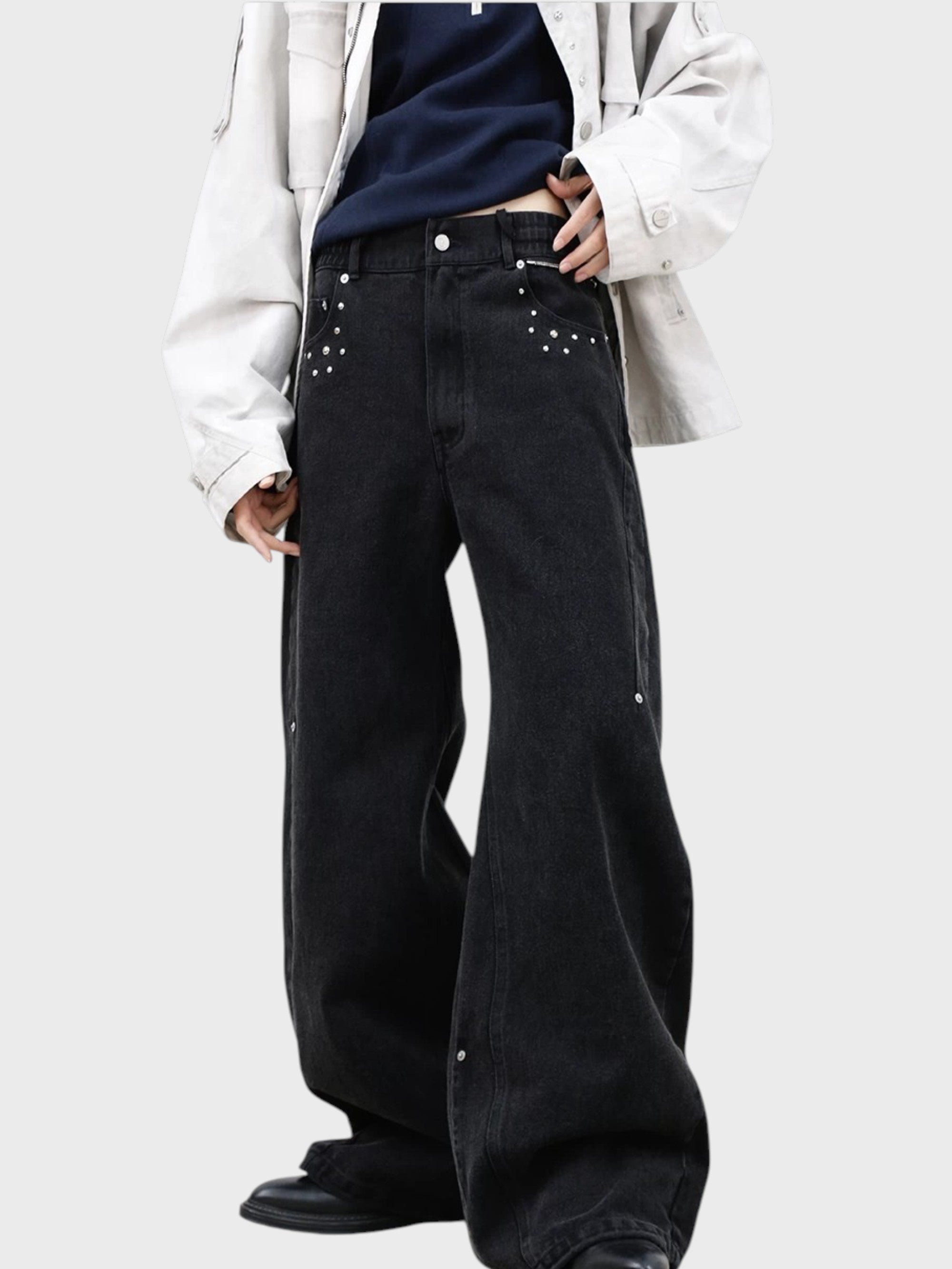 Jean large RELABEL noir washed porté, gros plan sur les rivets argentés constellation et les pinces inversées avec veste blanche et t-shirt marine
