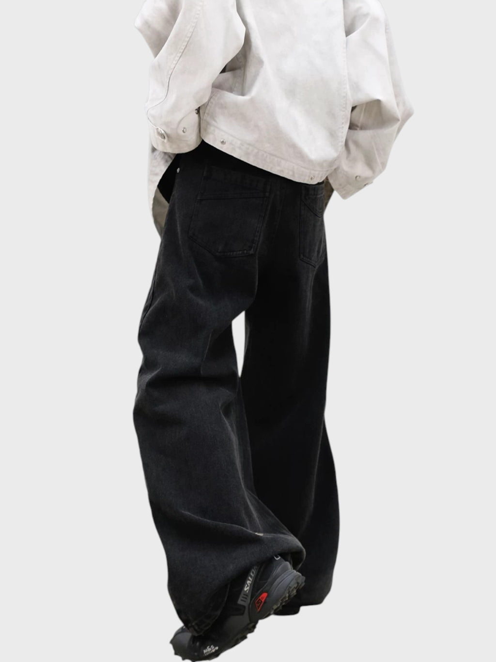 Jean large RELABEL noir washed porté de profil, silhouette A-line évasée avec veste blanche oversize et sneakers Salomon rouges

