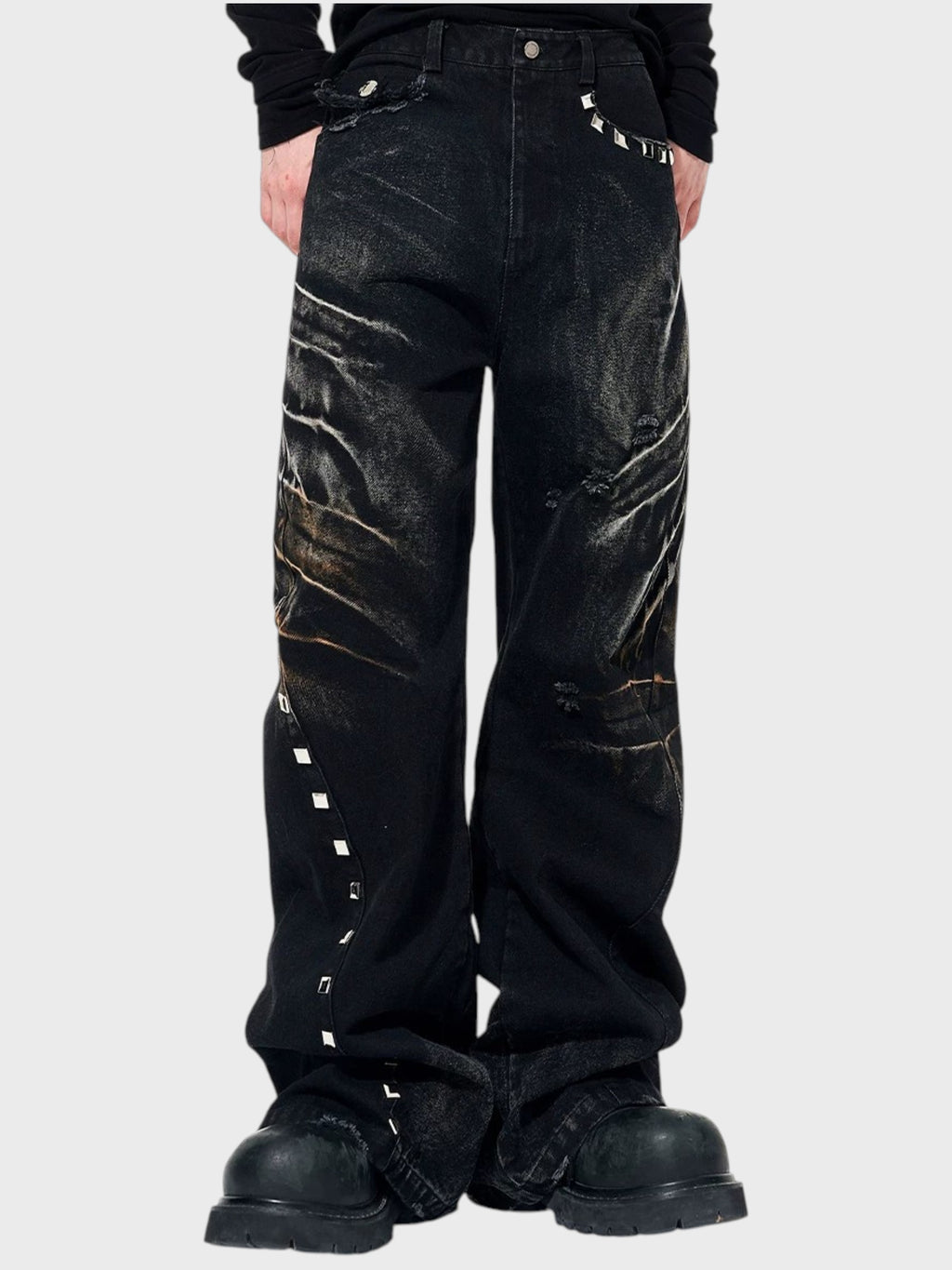 Jean large STARTEXCEEDEND noir washed porté par un homme, gros plan sur les rivets carrés argentés couture latérale et les déchirures brillantes avec pull noir et boots noires

