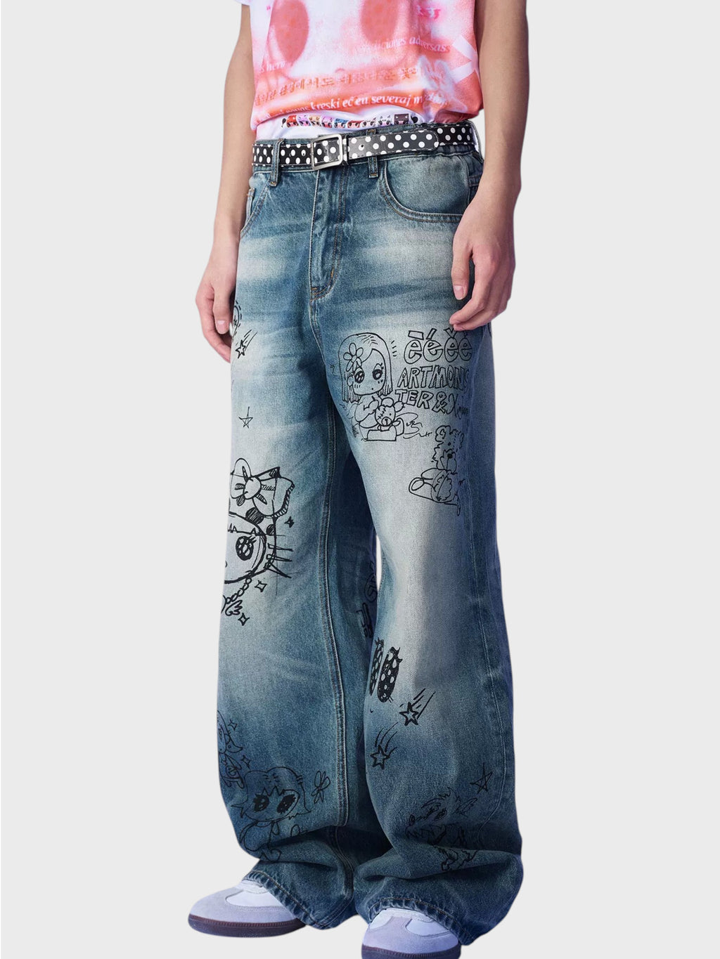 Jean large washed bleu eeee Artmonster porté par un homme, gros plan sur les imprimés graffiti manga et la ceinture à pois
