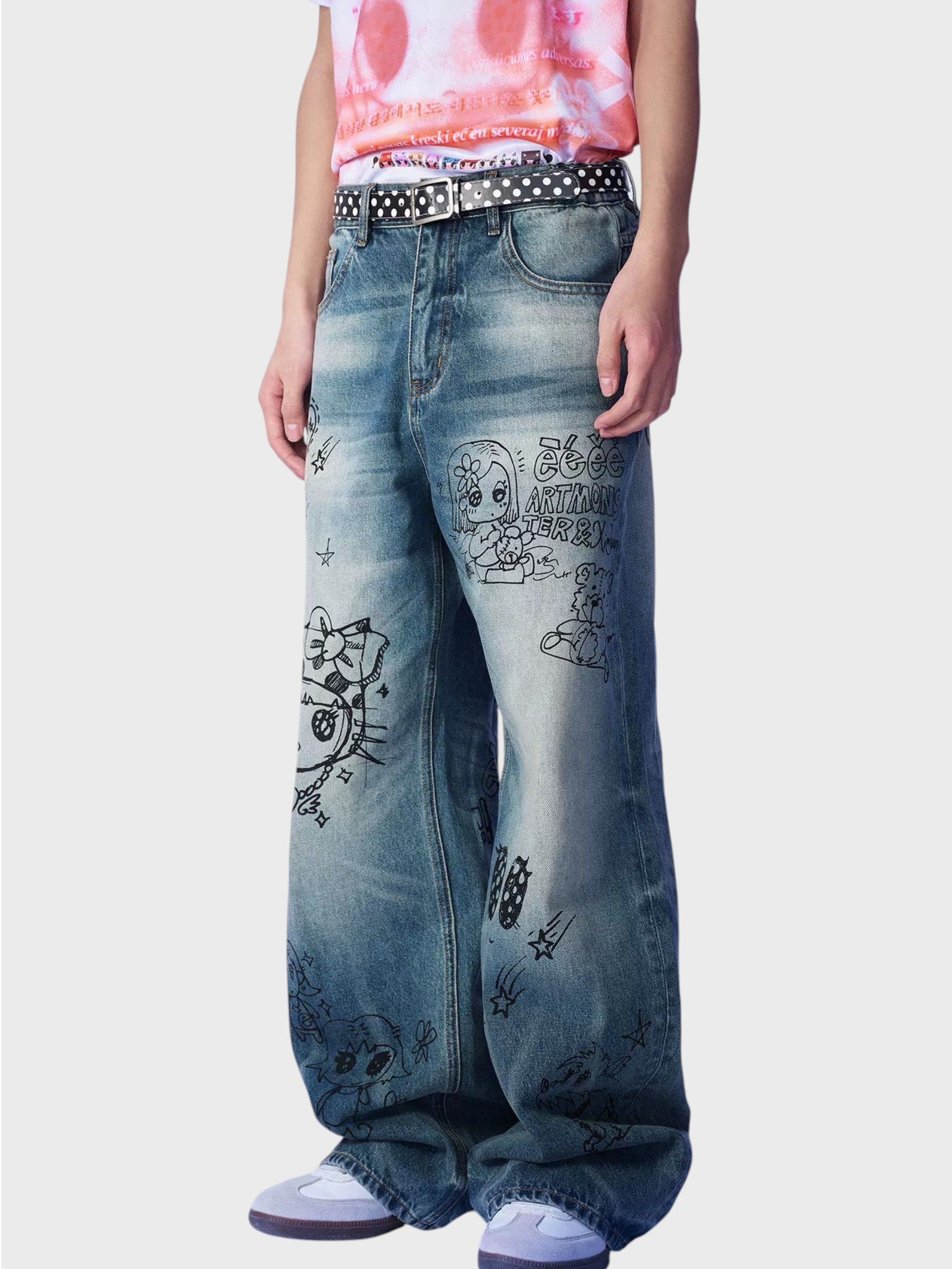 Jean large washed bleu eeee Artmonster porté par un homme, gros plan sur les imprimés graffiti manga et la ceinture à pois
