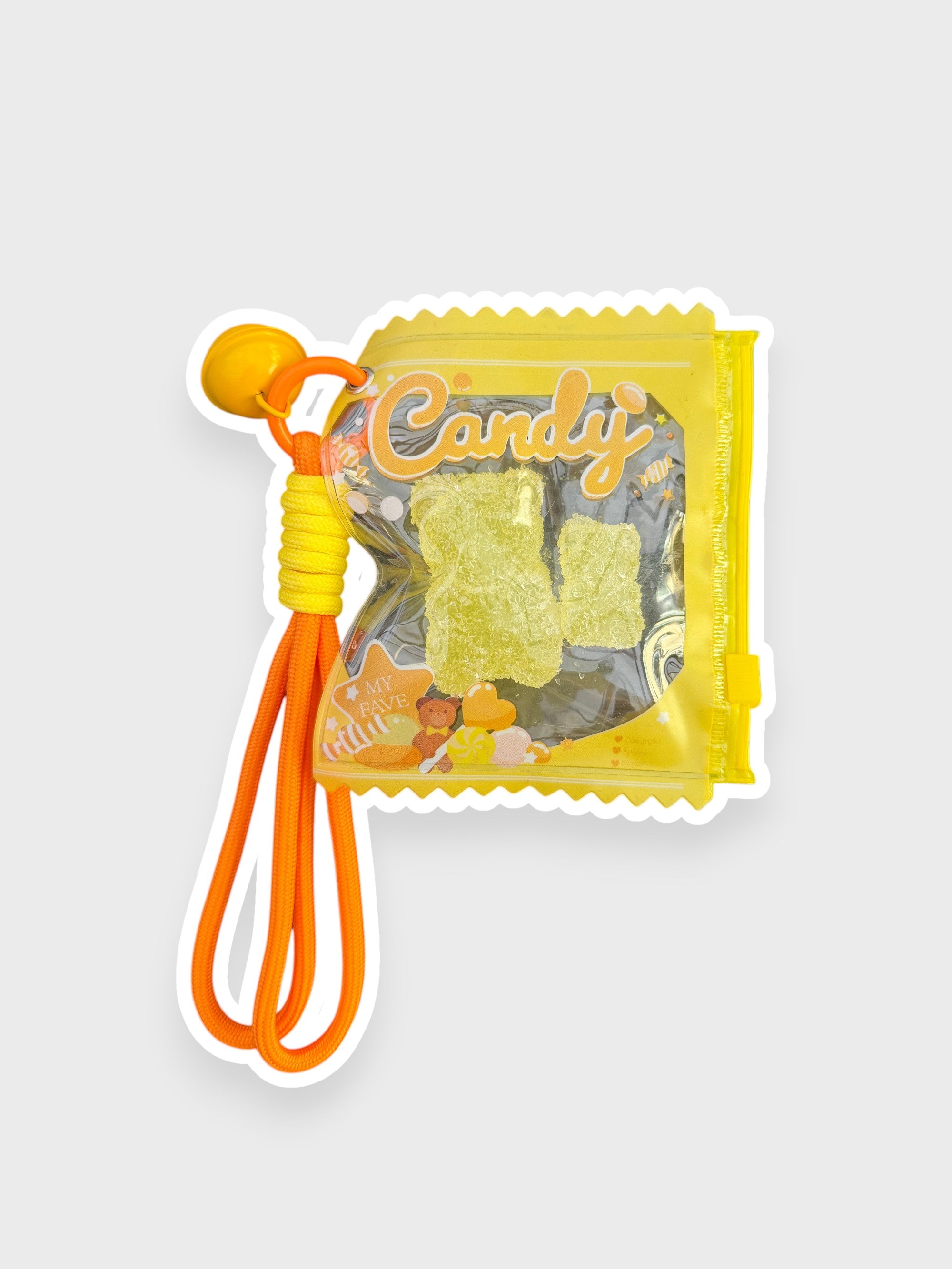 Jouet anti-stress ourson gélifiant ananas recouvert de sable scintillant jaune-vert givré dans sachet transparent jaune vif forme bonbon Candy lettrage doré avec lanterne cordon orange et perle orange, fond gris