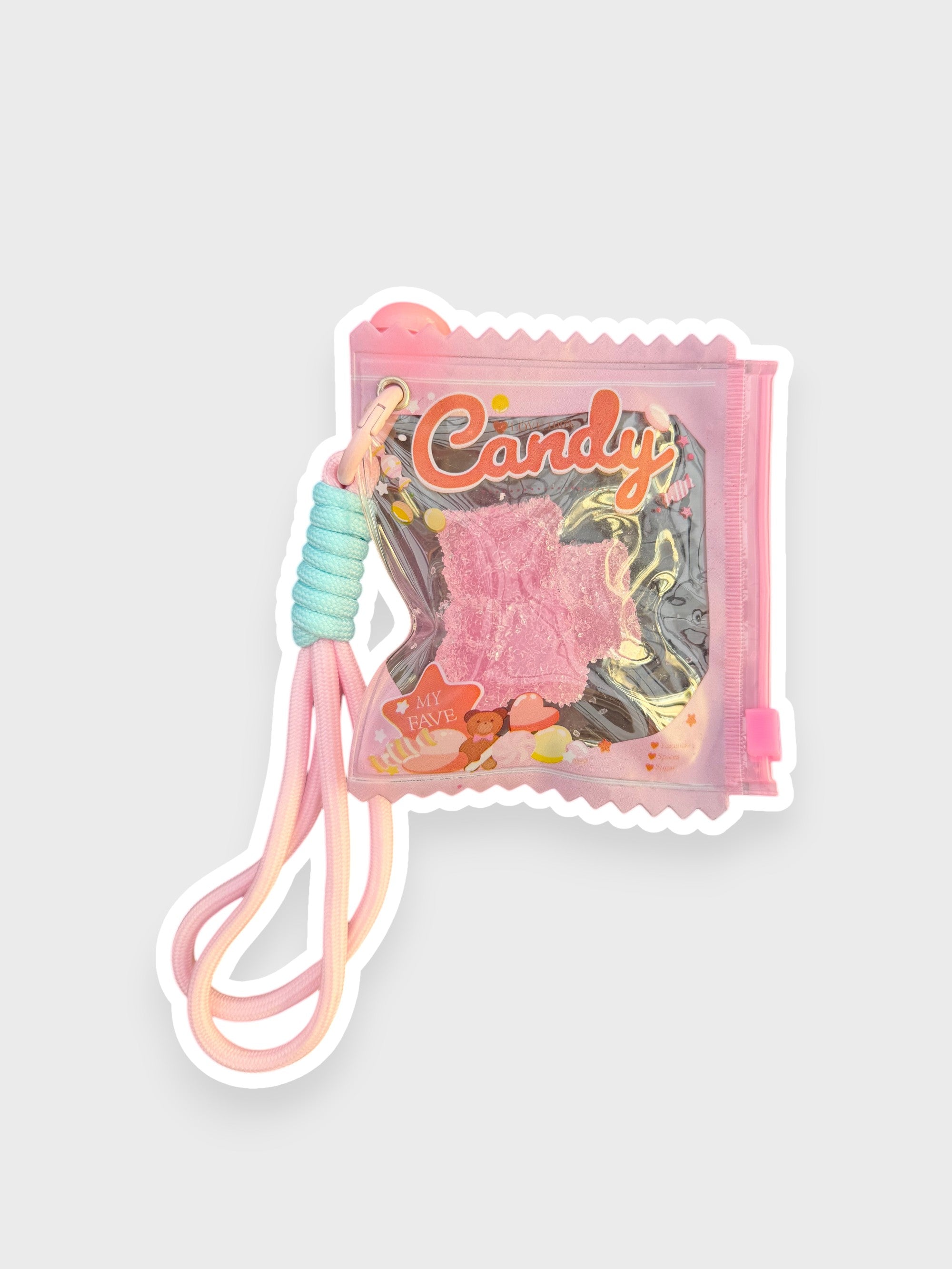 Jouet anti-stress ourson gélifiant fraise recouvert de sable scintillant rose givré dans sachet transparent iridescent rose forme bonbon Candy lettrage orange corail avec lanterne cordon rose dégradé, fond gris