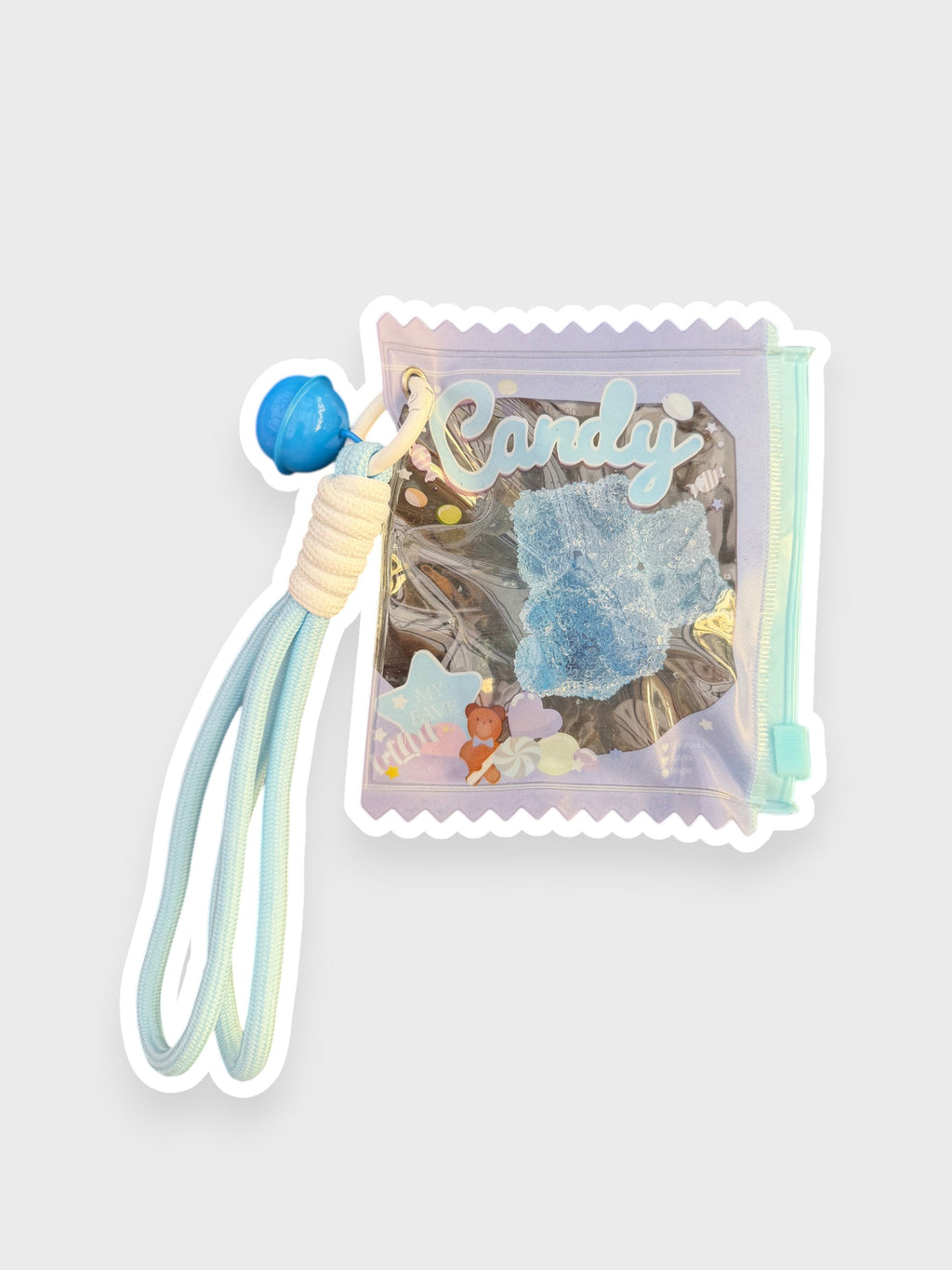 Jouet anti-stress ourson gélifiant myrtille recouvert de sable scintillant bleu givré dans sachet transparent iridescent forme bonbon Candy avec lanterne cordon bleu ciel, fond gris