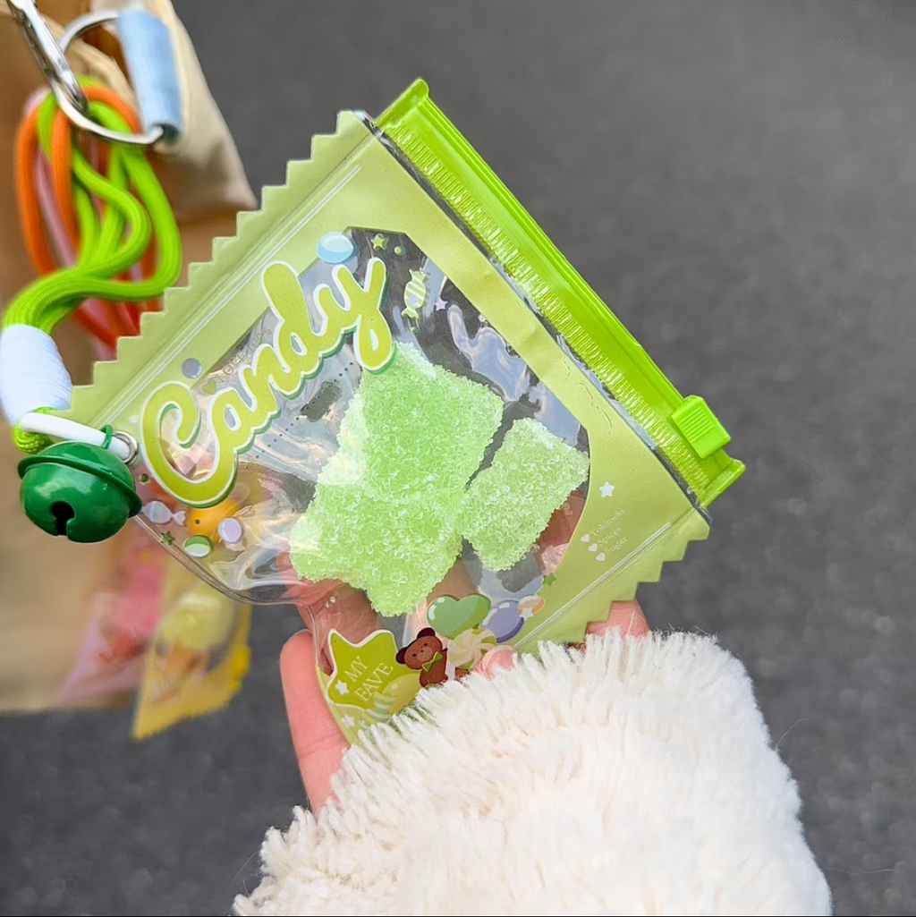 Jouet anti-stress ourson pomme sable scintillant vert tenu dans une main gantée blanc moelleux, sachet vert anis Candy zip vert avec grelot vert et cordon vert fluo, ambiance kawaii rue