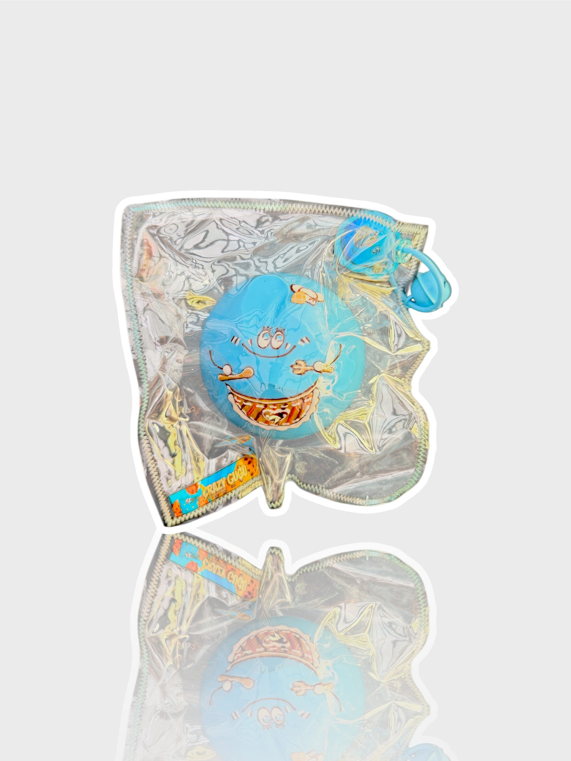 Jouet squishy mousse jelly Crazy Gugu bleu polyuréthane visage souriant, vue de face dans emballage holographique fond blanc
