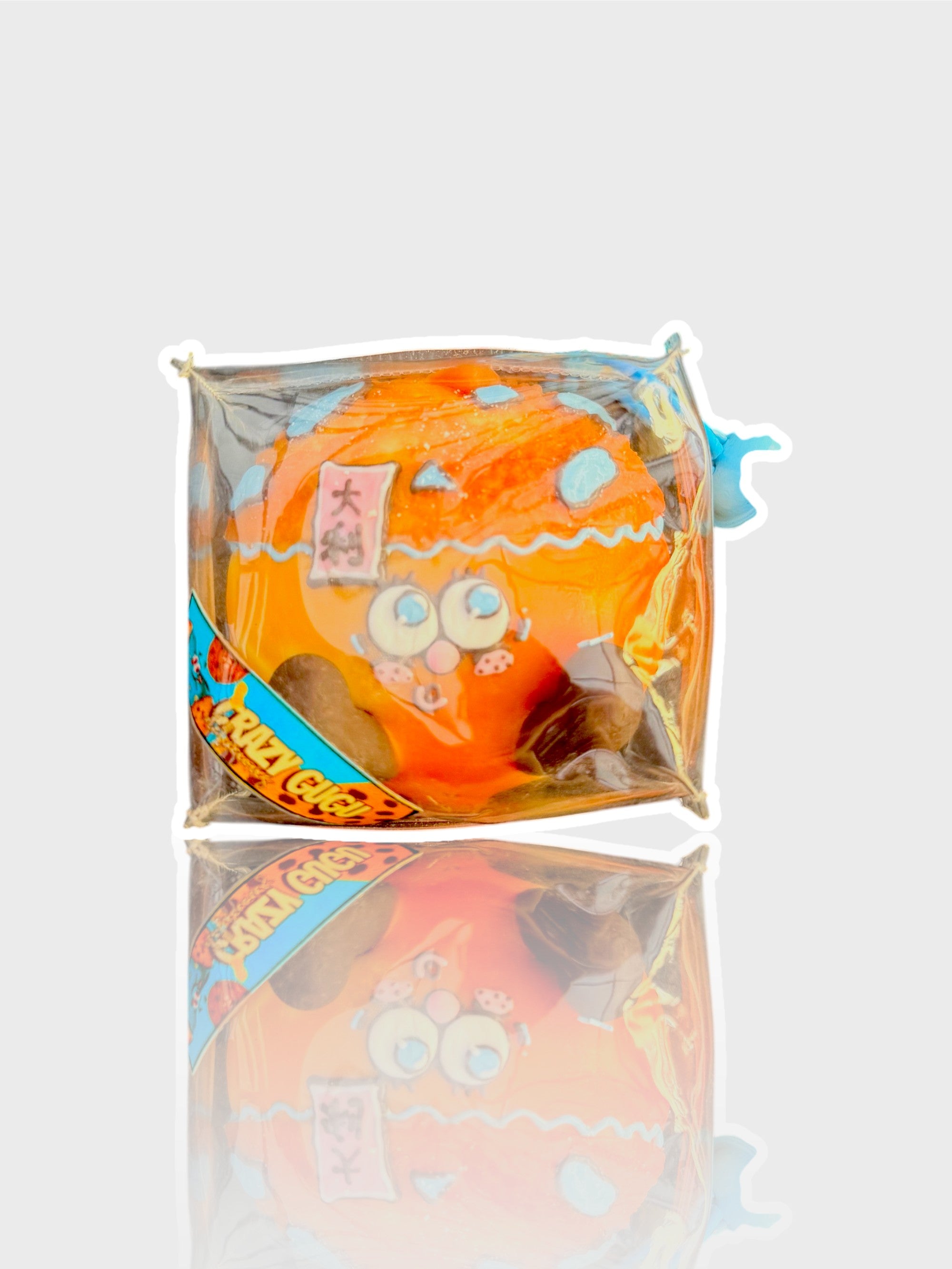 Jouet squishy mousse souple Crazy Gugu orange polyuréthane, vue de face dans emballage transparent fond blanc