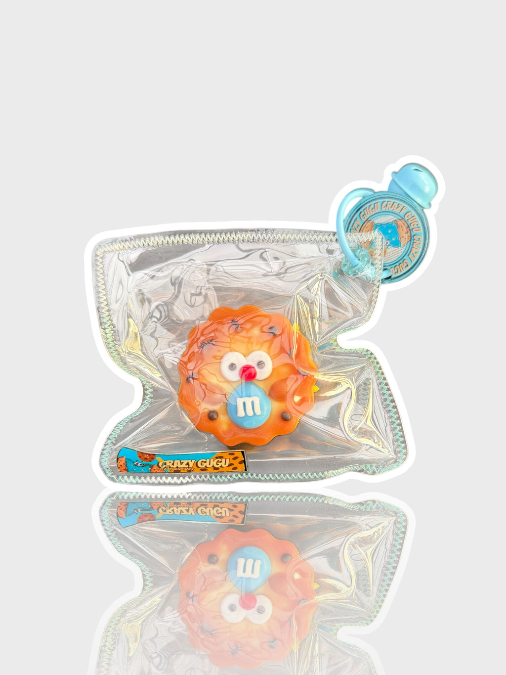 Jouet squishy texture cookie Crazy Gugu orange et bleu polyuréthane M&M, vue de face dans emballage holographique fond blanc