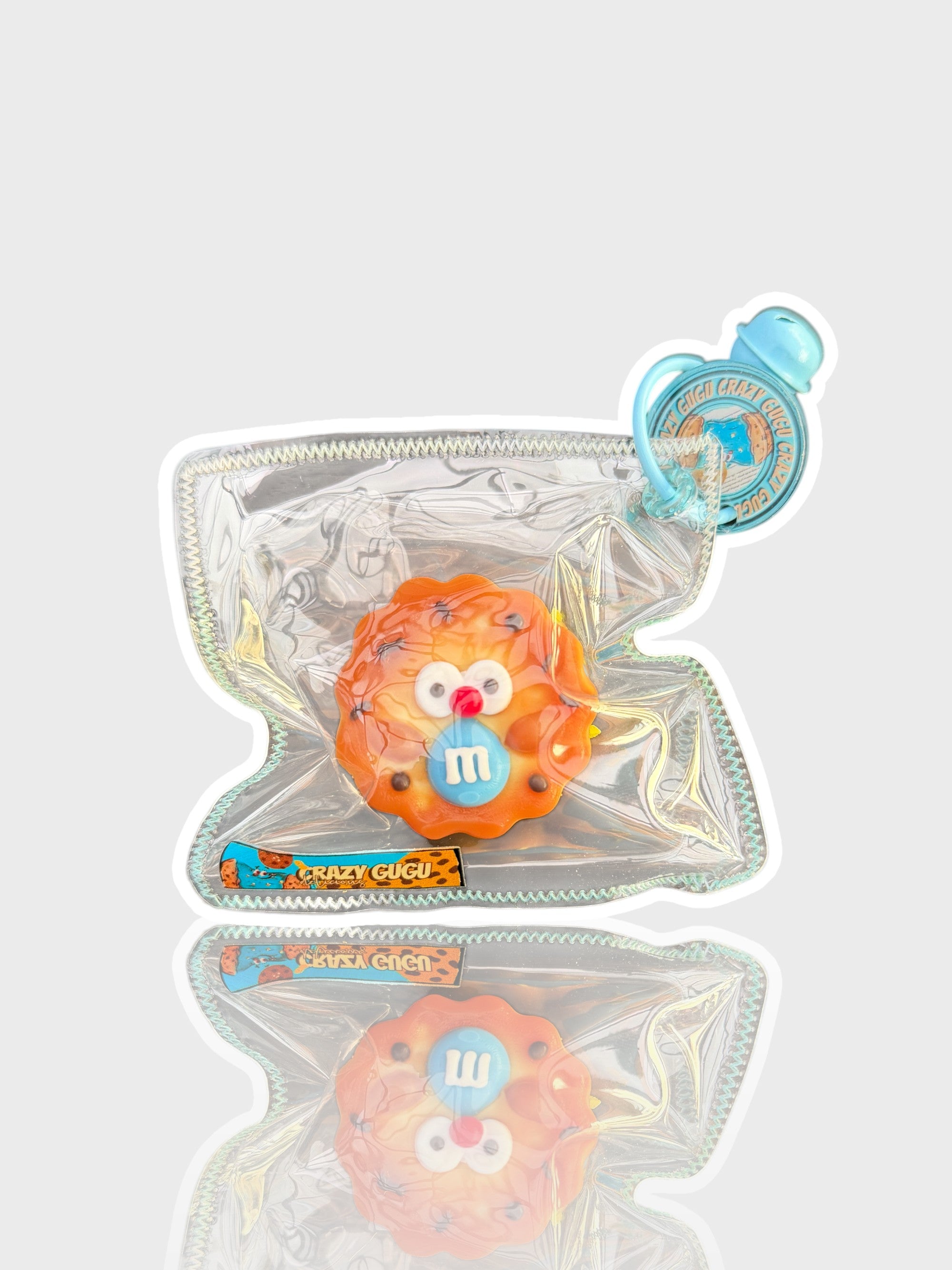 Jouet squishy texture cookie Crazy Gugu orange et bleu polyuréthane M&M, vue de face dans emballage holographique fond blanc