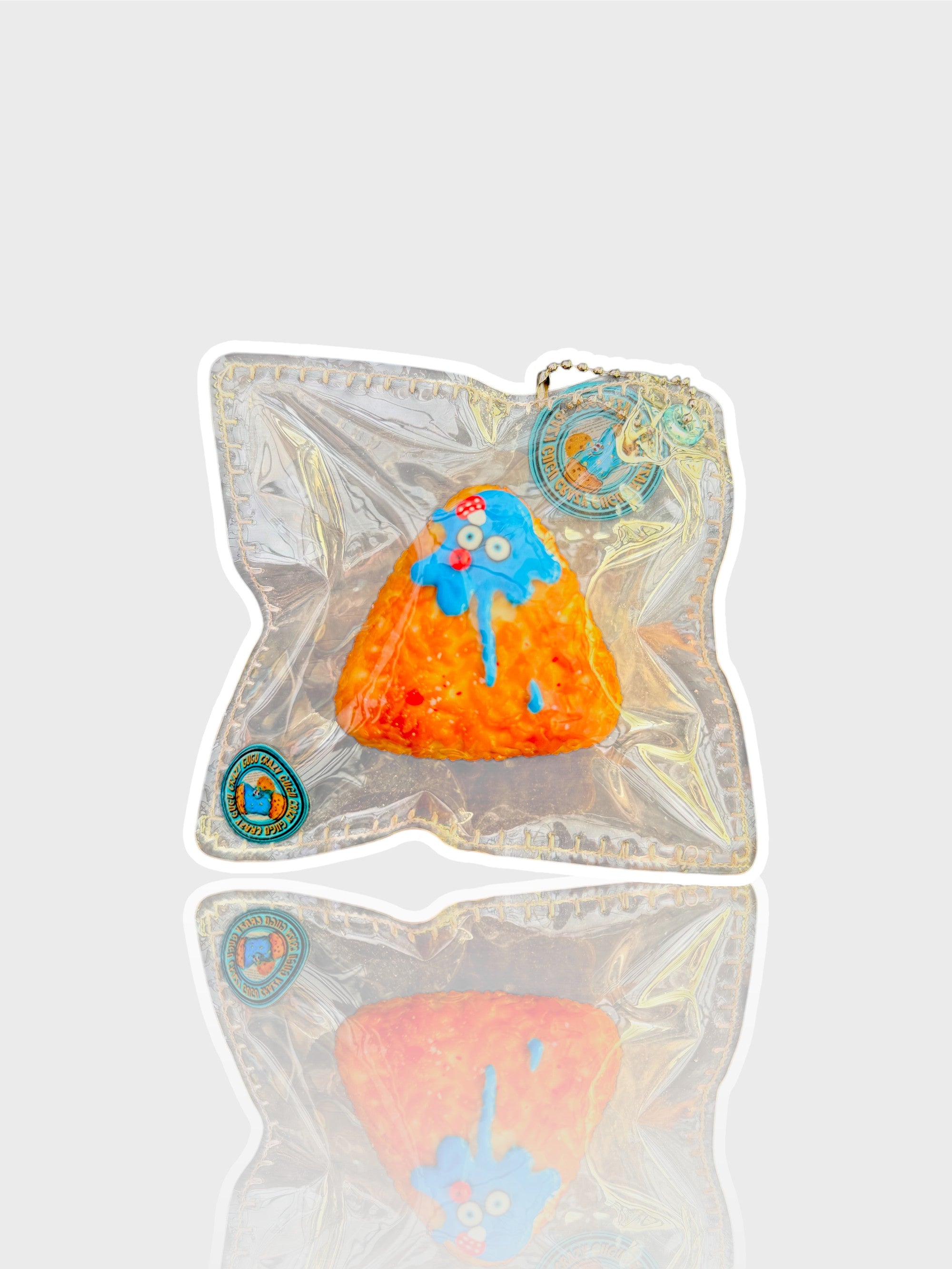 Jouet squishy texture riz Crazy Gugu orange et bleu polyuréthane onigiri monstre, vue de face dans emballage holographique fond blanc