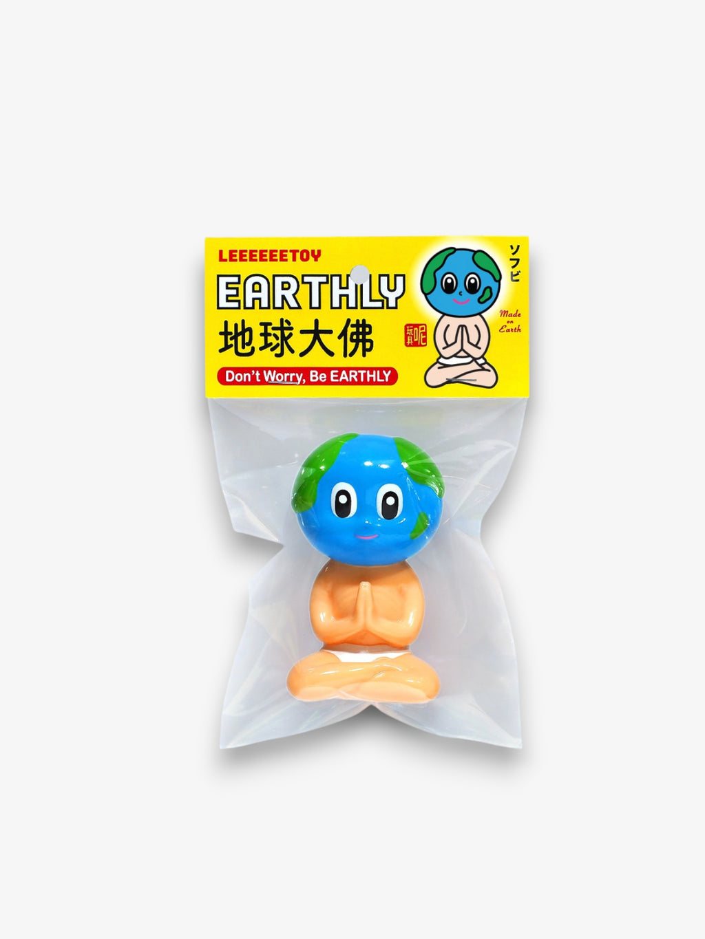 Leeeeeetoy Earthly  sofubi figurine – personnage méditant en position lotus corps beige avec tête globe terrestre bleu et vert, packaging sachet transparent étiquette jaune "Don't Worry, Be Earthly"
