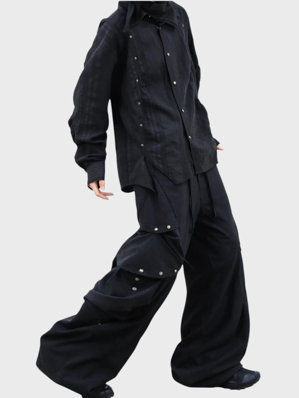 Pantalon déconstructiviste RELABEL noir porté par une femme de profil, avec veste noire boutons-pression et poches cargo déployées
