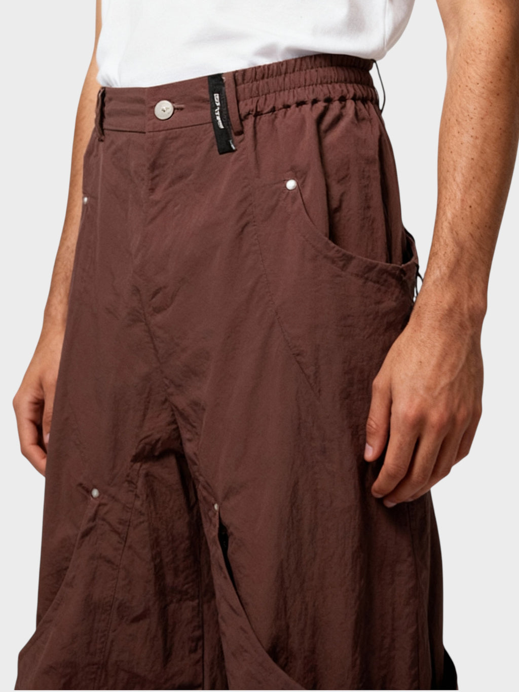 Pantalon cargo multi-poches zippées Relabel bordeaux en nylon, porté par un homme, vue rapprochée détail taille et poches sur fond gris