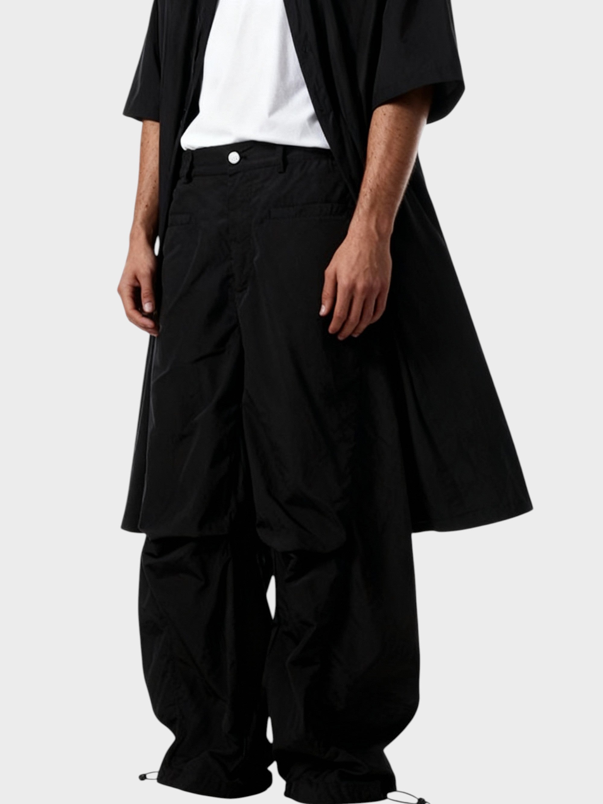 Pantalon cargo superposé avec jupe Relabel noir en nylon, porté par un homme en studio sur fond gris, vue rapprochée détail jupe évasée superposée et bouton pression