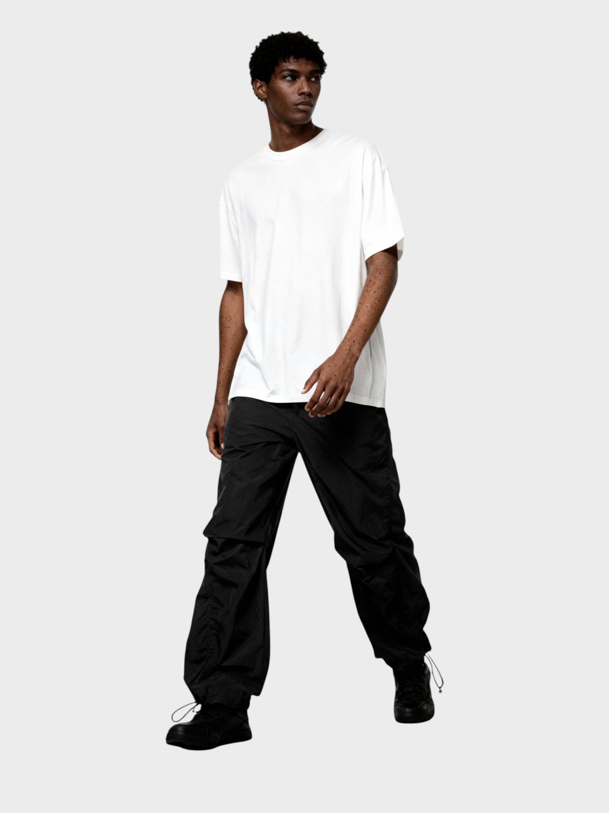 Pantalon cargo superposé avec jupe Relabel noir en nylon, porté par un homme avec un t-shirt blanc oversize en studio sur fond gris, vue de face silhouette complète
