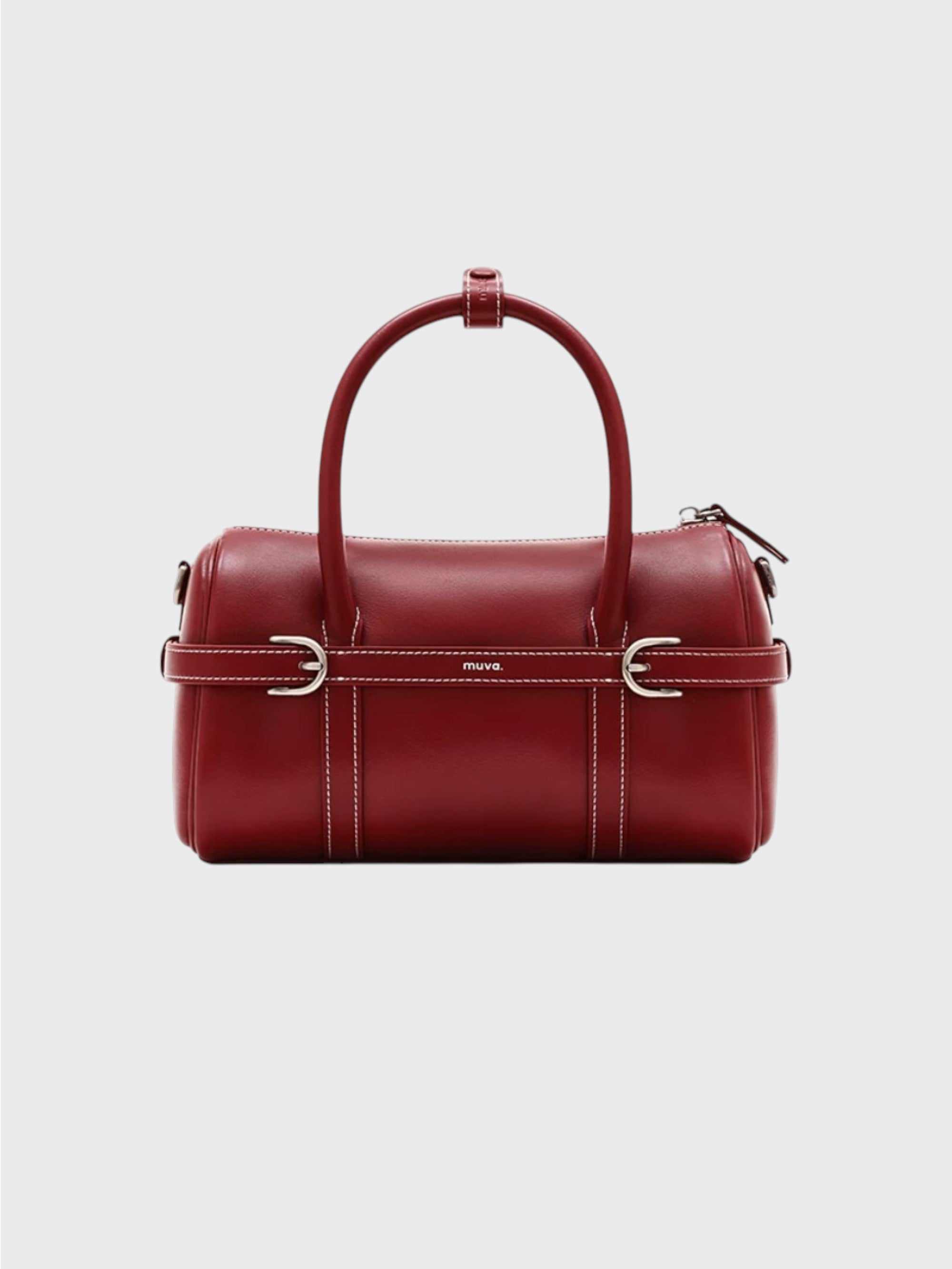 Sac boston MUVA cuir véritable rouge bordeaux avec surpiqûres blanches, sangle centrale boucles D argentées et logo MUVA gravé, anse arrondie rigide, vue de face fond gris
