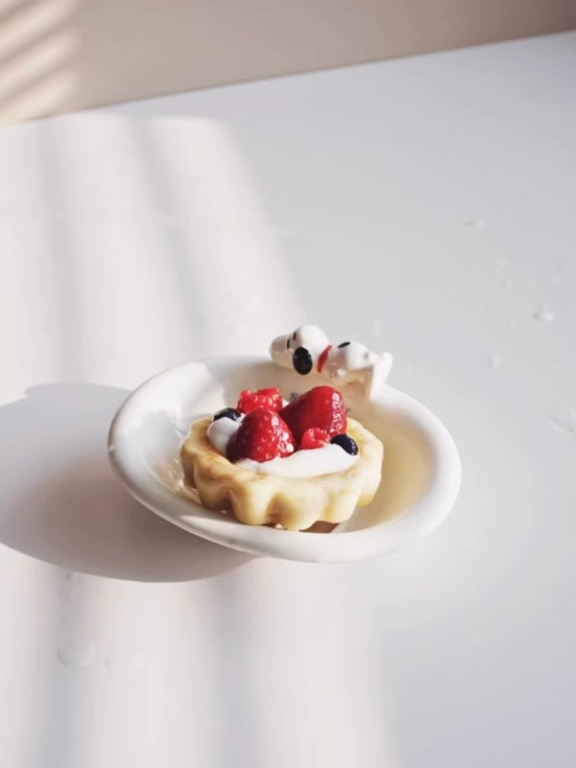 Savon artisanal en forme de tarte aux fraises et myrtilles avec figurine Snoopy, posé sur une assiette en céramique blanche, photo lifestyle sur fond blanc
