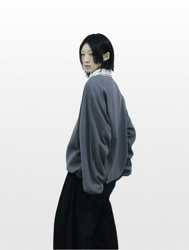 Sweat polo demi-zip oversize RELABEL gris col blanc porté par une femme de profil, avec pantalon large noir et chemise blanche en dessous

