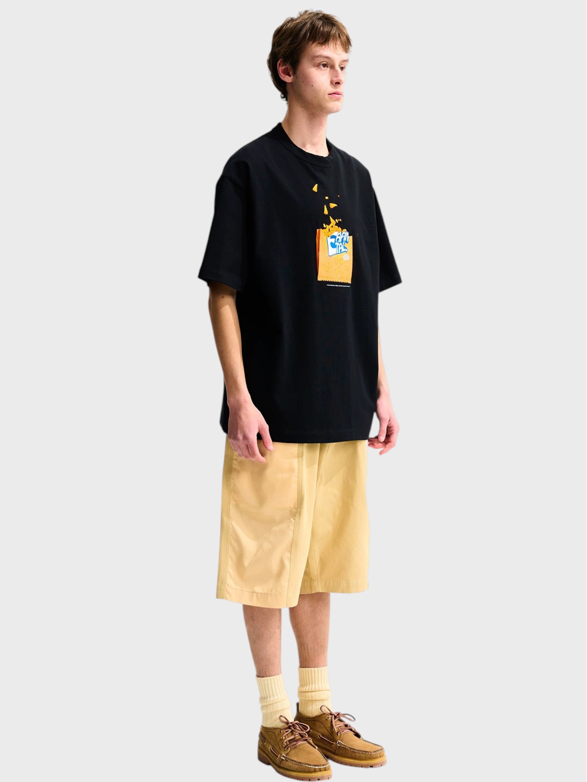 T-shirt oversize EAFINETAL. noir brodé Doritos flammes porté par un homme, look complet avec short large beige, chaussettes blanches et chaussures bateau marron, vue de trois quarts
