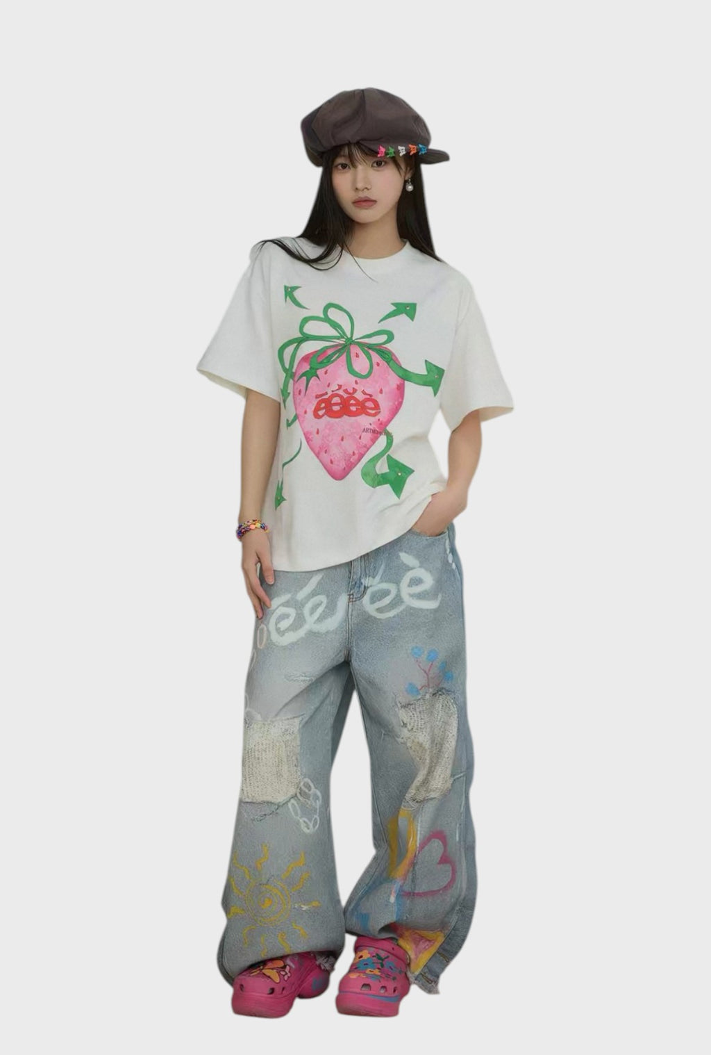 T-shirt oversize eeee Artmonster blanc imprimé fraise rose porté par une femme, look complet avec jean large graffiti bleu washed et crocs roses plateforme, vue de face