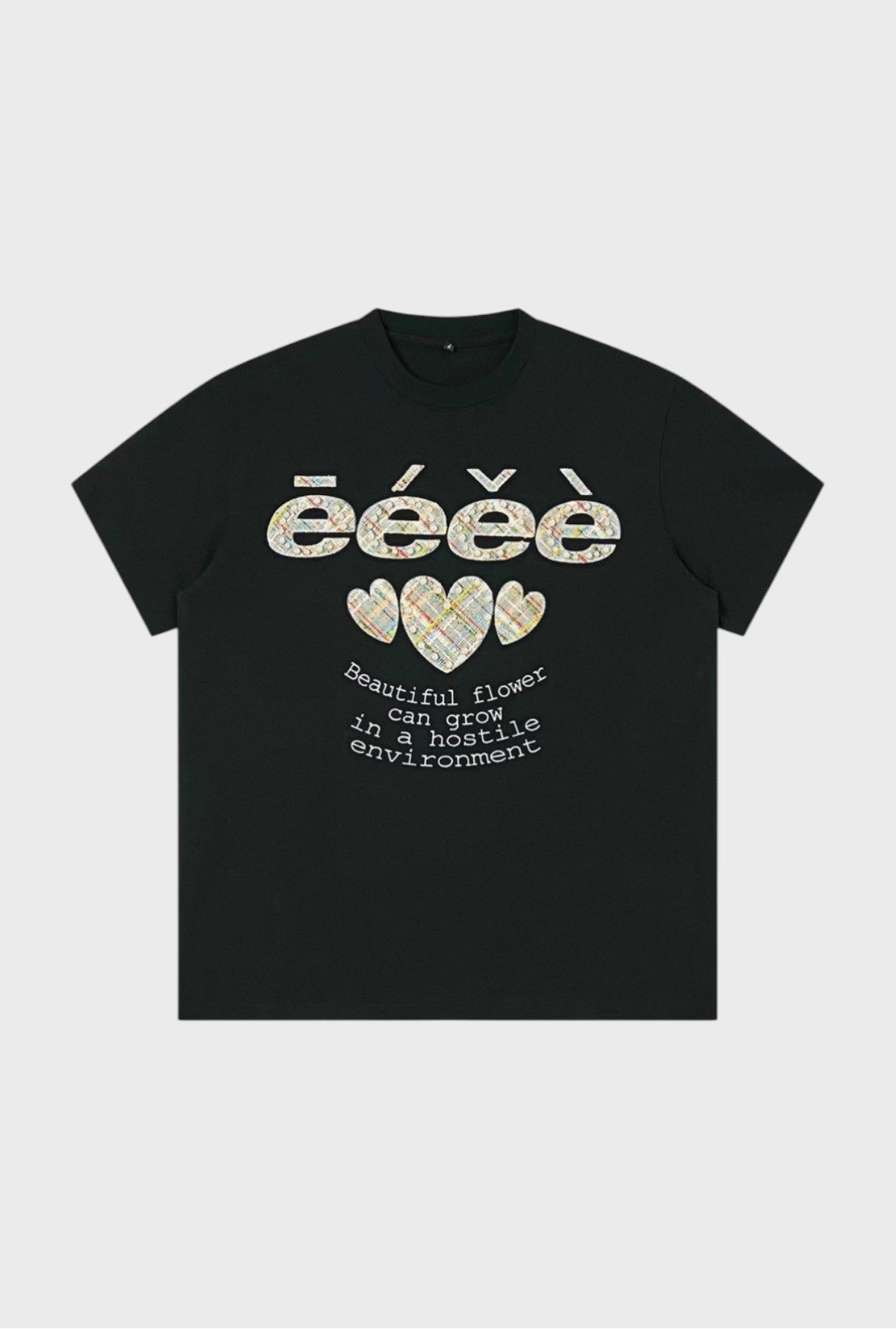 T-shirt oversize eeee Artmonster noir avec appliqués tweed multicolore logo eeee et trois cœurs perles, inscription "Beautiful flower can grow in a hostile environment", vue de face