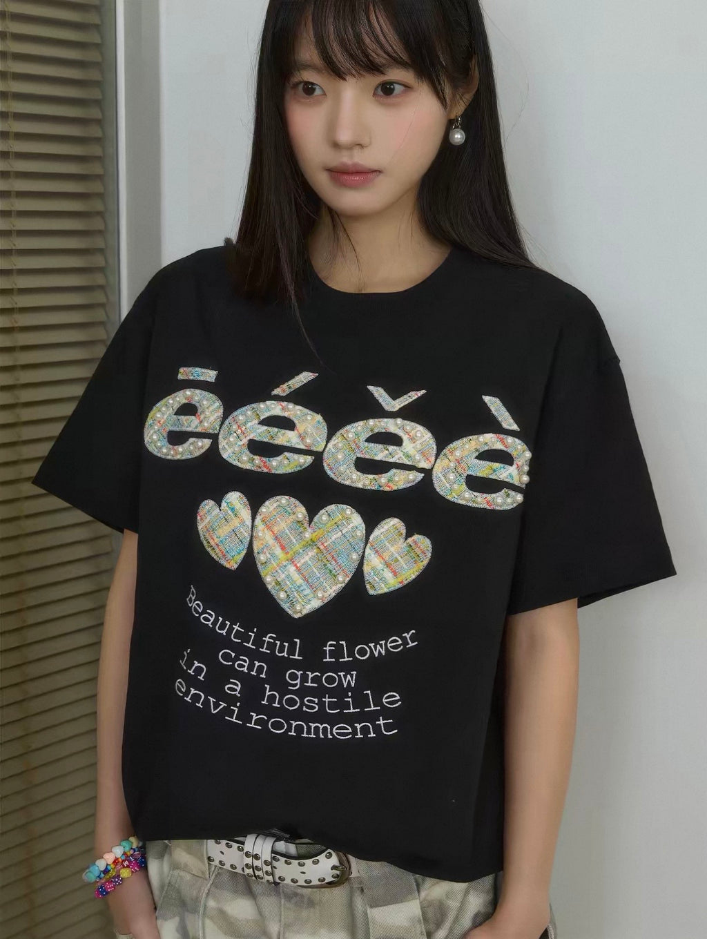 T-shirt oversize eeee Artmonster noir appliqués tweed multicolore et perles porté par une femme avec ceinture blanche rivets et short camouflage, vue de face